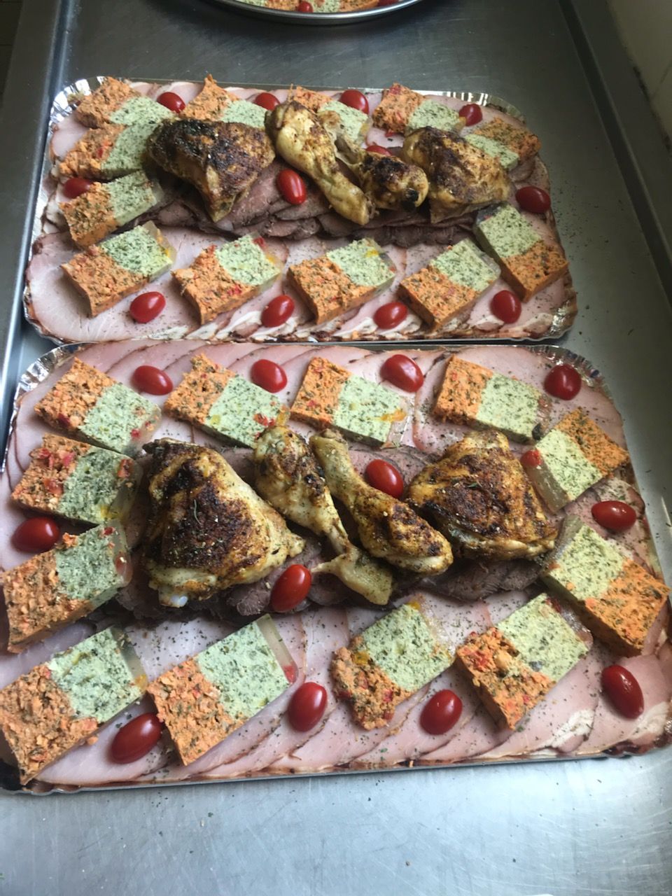 Deux plateaux de nourriture : jambon tranché, moitiés de tomates, carrés de pain colorés et morceaux de poulet rôti.