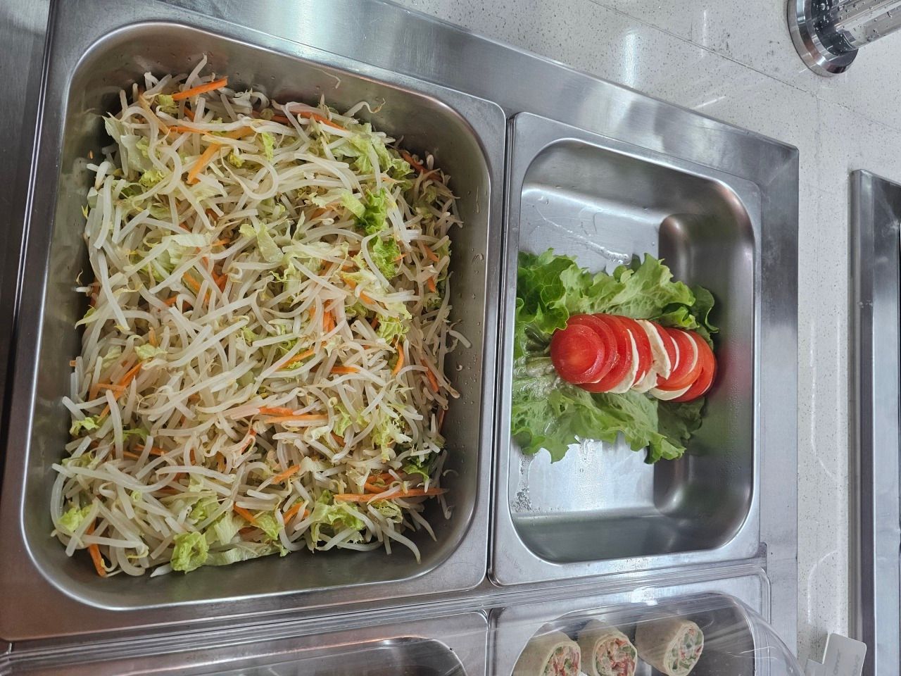 Un récipient rempli d'une salade de légumes râpés, à côté d'un petit bol de tomates et de laitue coupées en tranches.