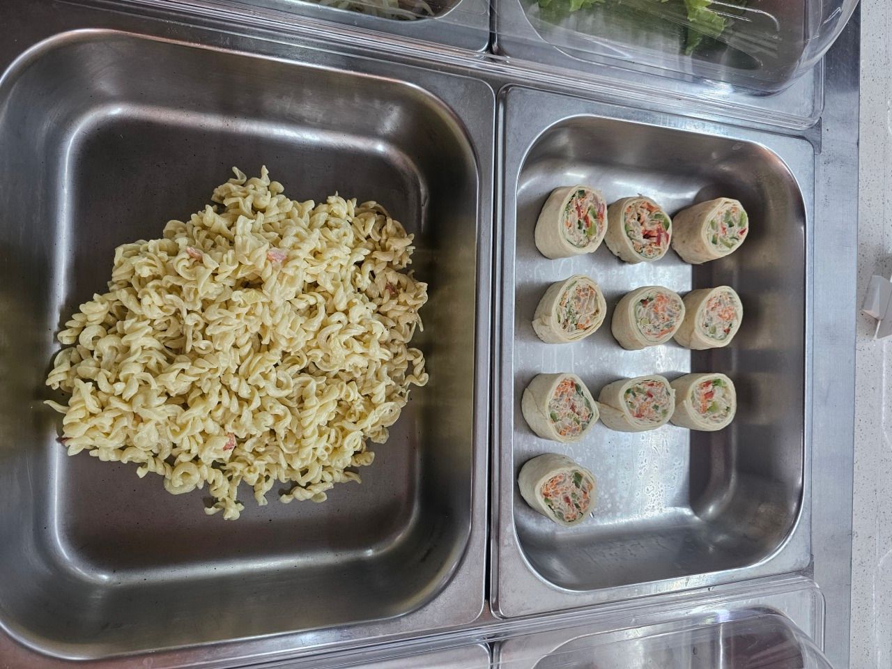 Bacs alimentaires en acier, l'un contenant une salade de pâtes et l'autre dix petits roulés de pâte à frire tranchés.