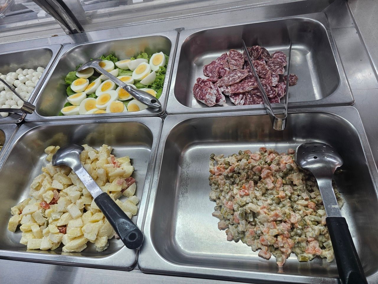 Quatre plats de buffet en métal remplis d'œufs durs tranchés, de salami, de salade de pommes de terre et de salade.