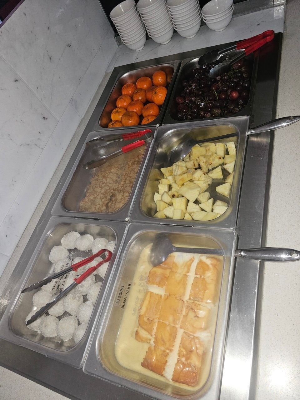 Vue en plongée d'un buffet composé de six récipients contenant des fruits, des noix, des desserts et des boules blanches.