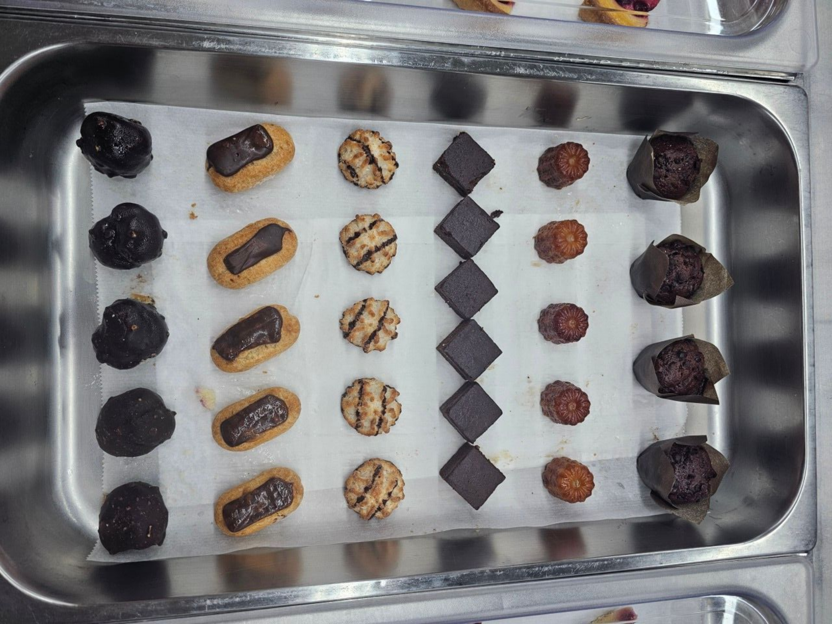Un plateau en métal recouvert de papier sulfurisé, contenant six rangées de pâtisseries miniatures variées.