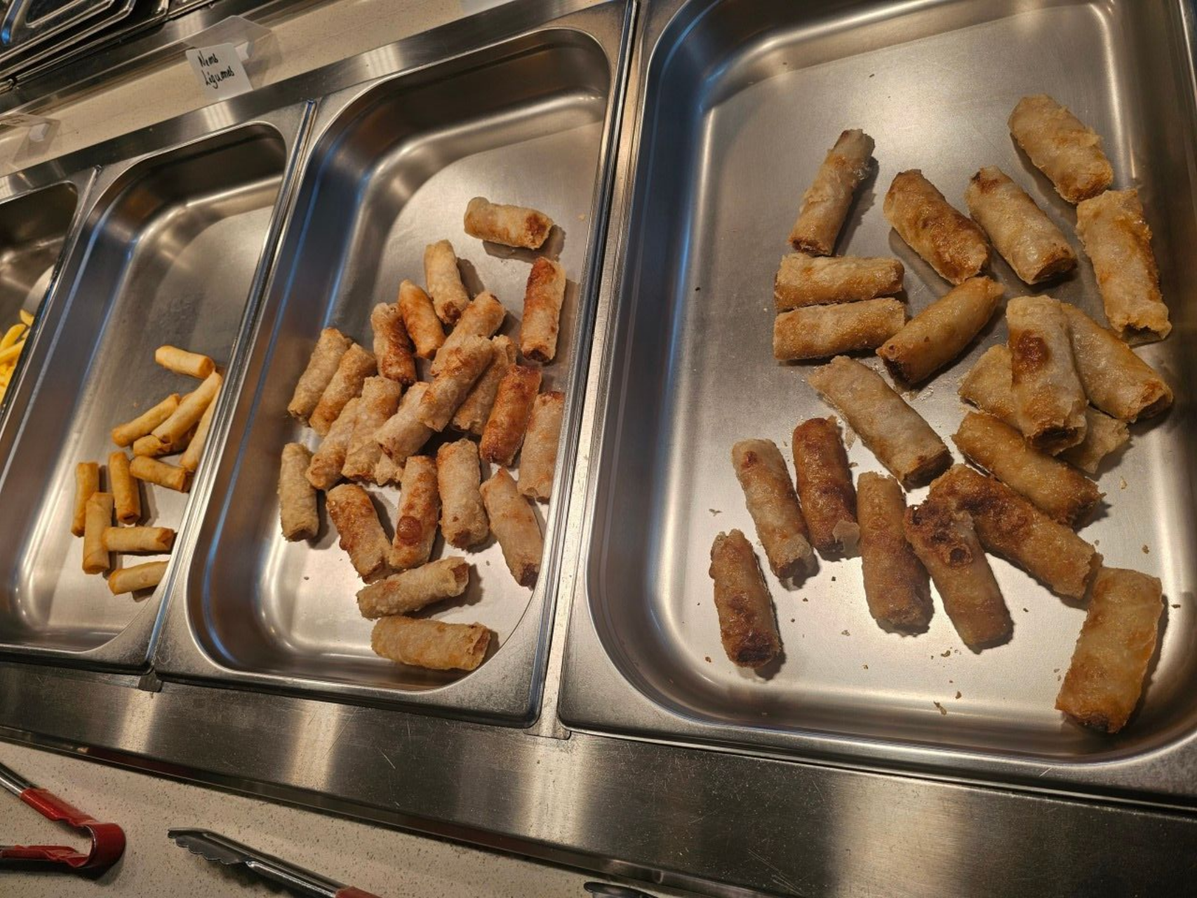 Trois plateaux métalliques remplis de rouleaux de printemps croustillants et dorés, dans un chauffe-plats de type cafétéria.