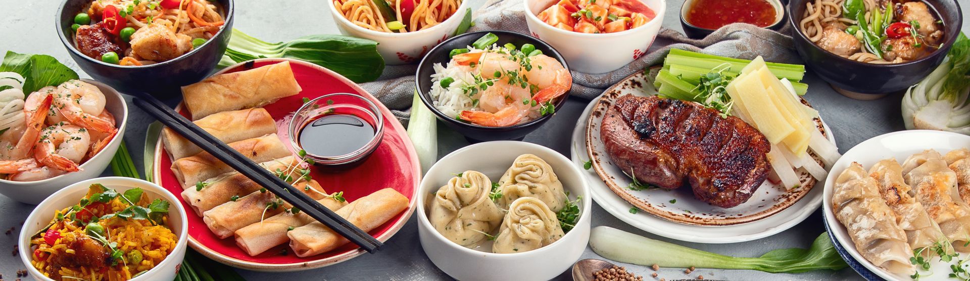 Un assortiment de plats asiatiques, des bols de nouilles, des rouleaux de printemps, des raviolis et de la viande grillée.