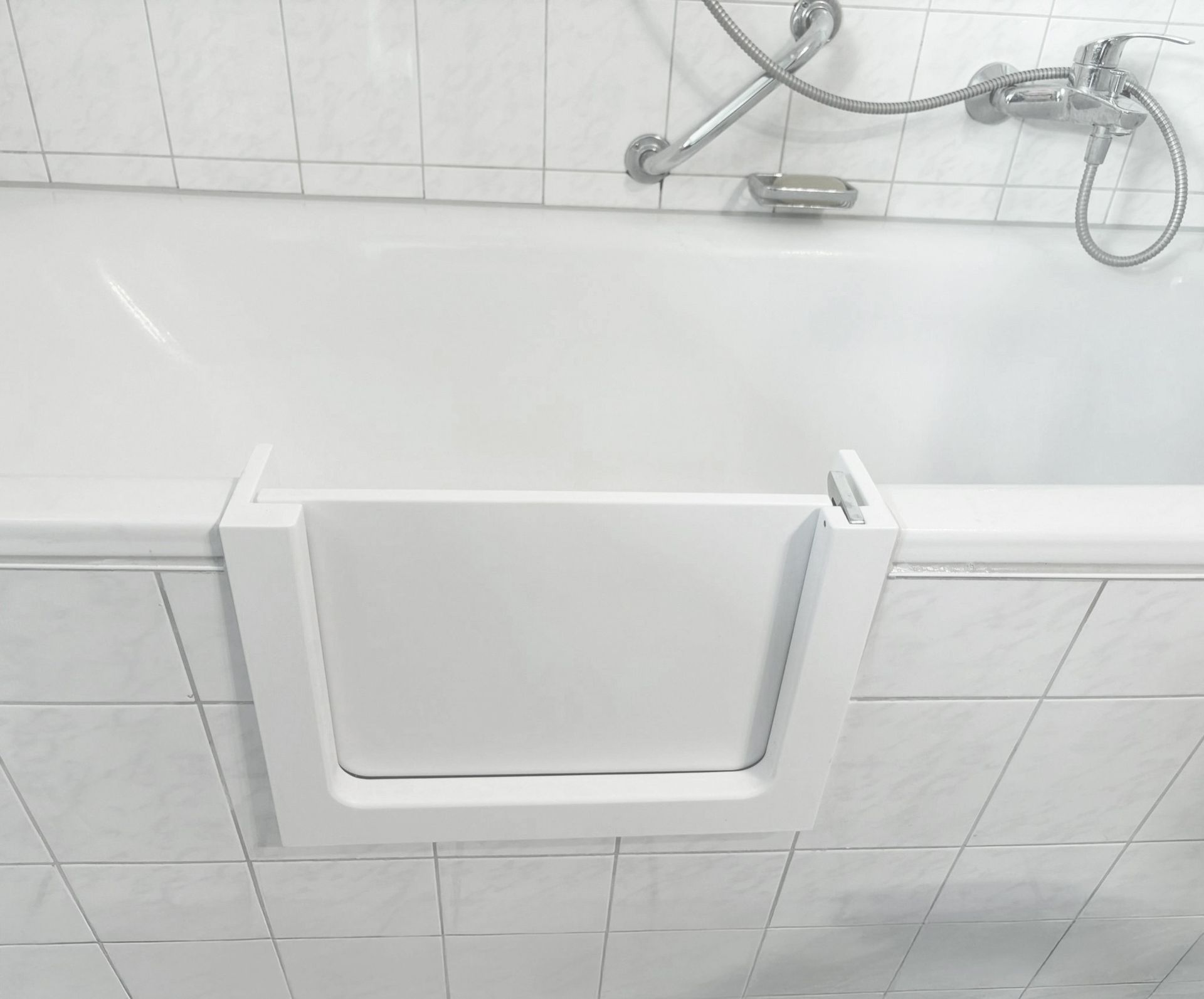 Weißer, klappbarer Duschsitz, montiert in einem gefliesten Badezimmer unter einer Handbrause.