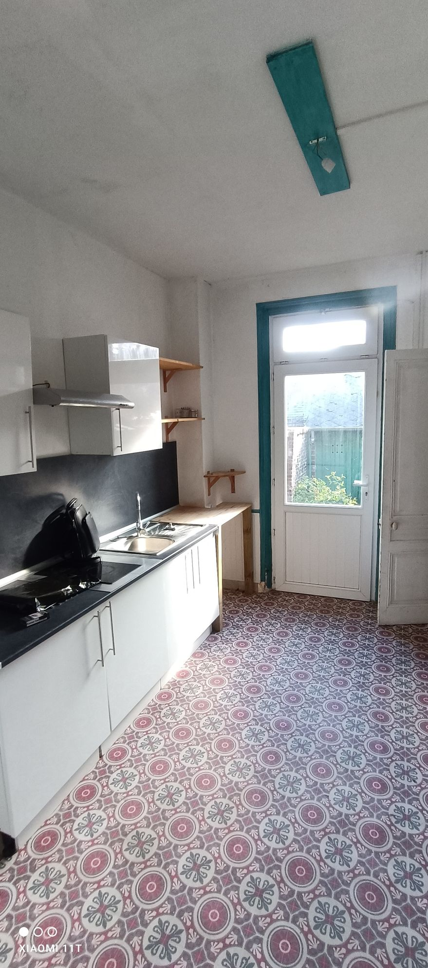 Cuisine avec placards blancs, sol à motifs et porte donnant sur l'extérieur.