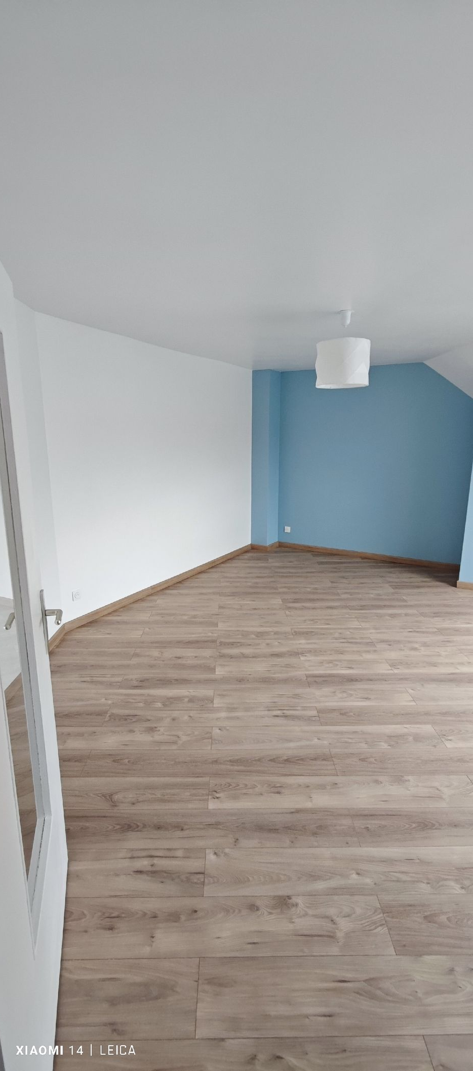 Une pièce vide avec un mur bleu, des murs blancs et un parquet clair.