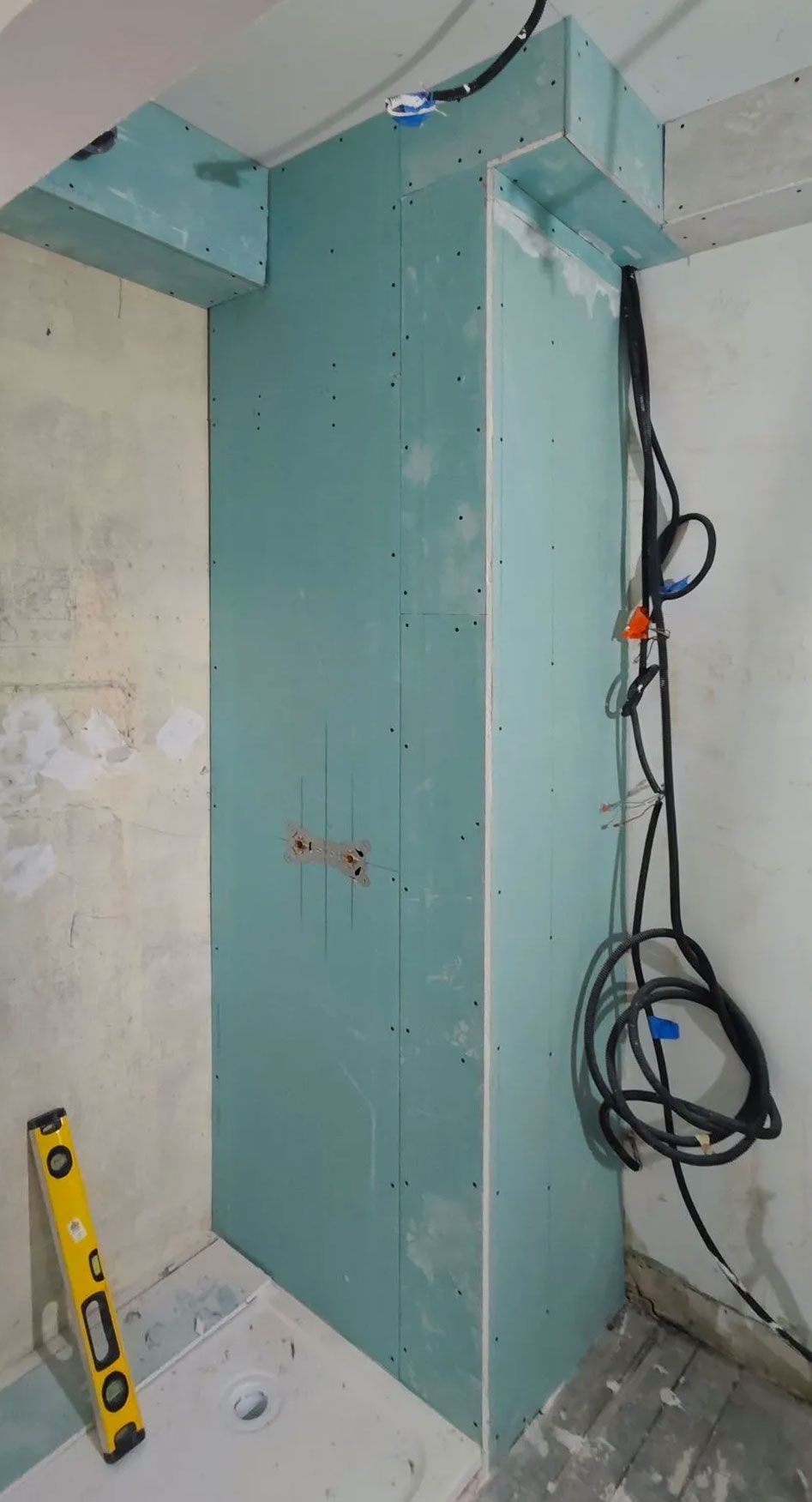 Un mur partiellement construit dans une pièce, avec des fils électriques et un niveau.