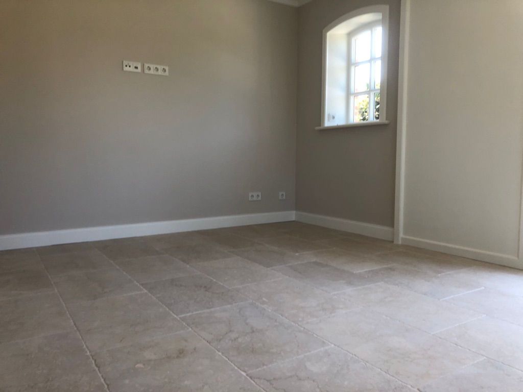 Leerer Raum mit hellem Fliesenboden, beigen Wänden und Bogenfenster. Weiße Zierleisten.