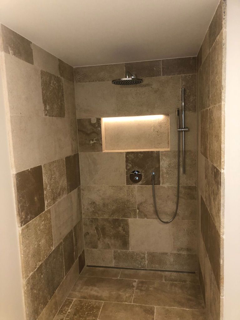 Duschkabine mit beigen Steinfliesen, eingebauter Nische mit Licht und silbernem Duschkopf und Handbrause.
