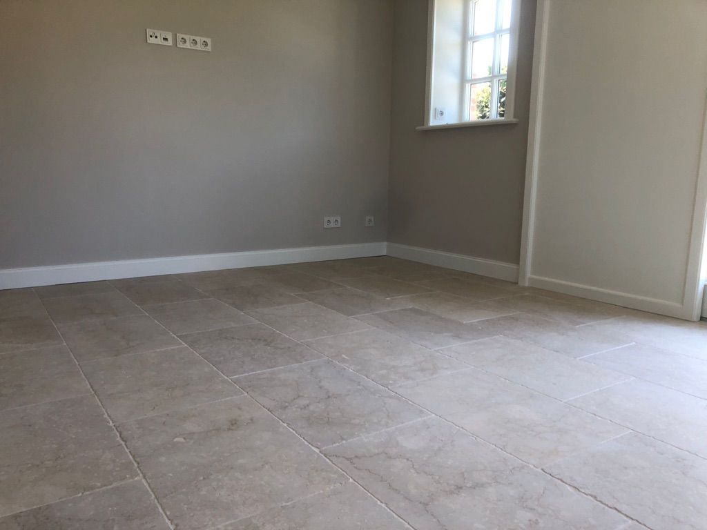 Leerer Raum mit beigem Fliesenboden, grauen Wänden, weißen Zierleisten und einem Fenster.