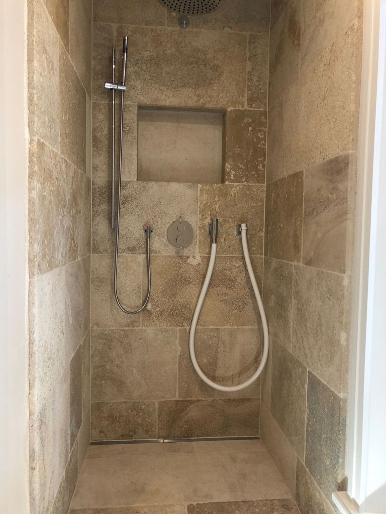 Duschkabine mit beigen Steinfliesen und silbernen Armaturen.