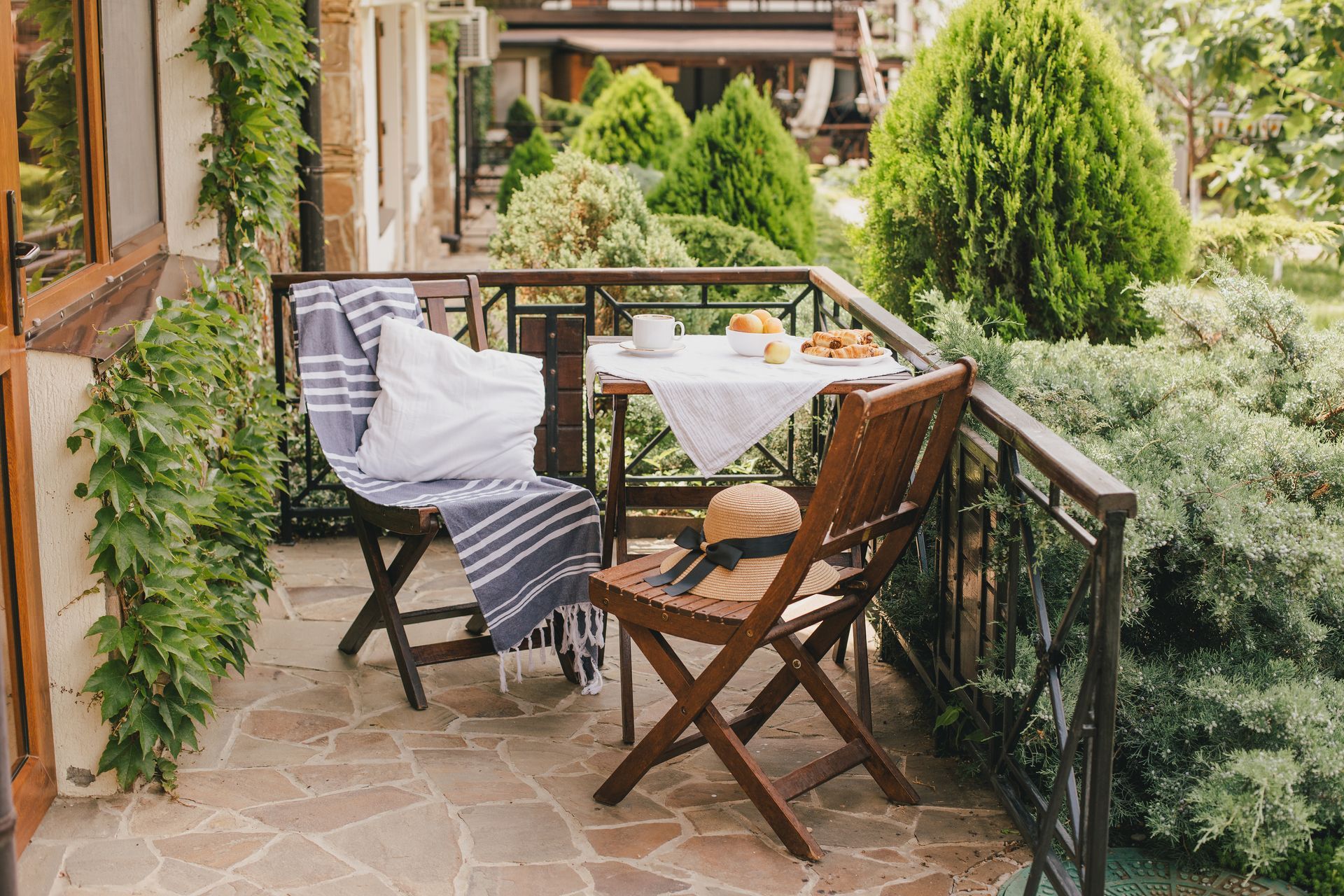 Balkon mit gedecktem Frühstückstisch, zwei Stühlen und üppigem Grün.