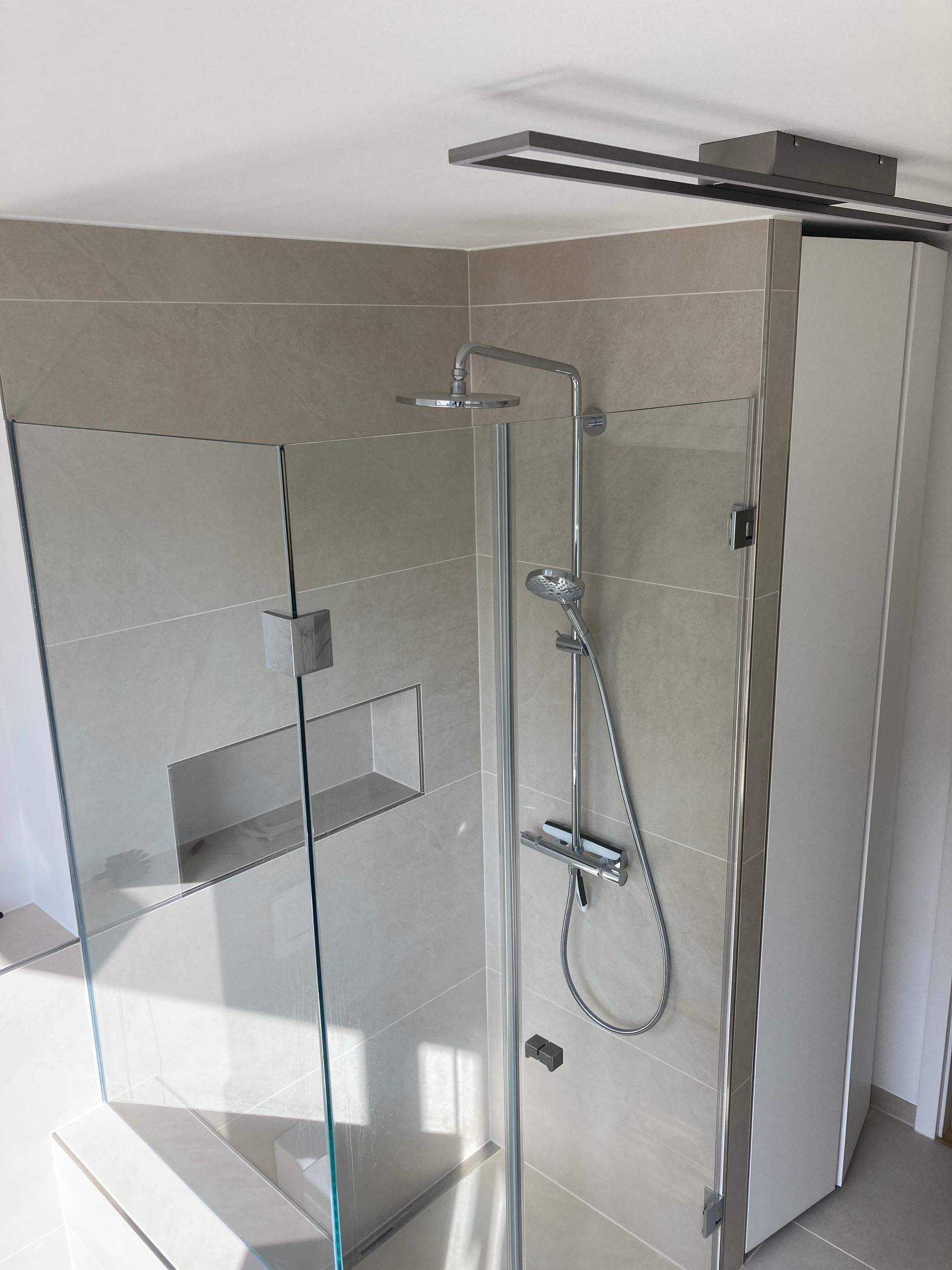Moderne Dusche mit Glastür, silbernen Armaturen, hellbeige gefliesten Wänden.