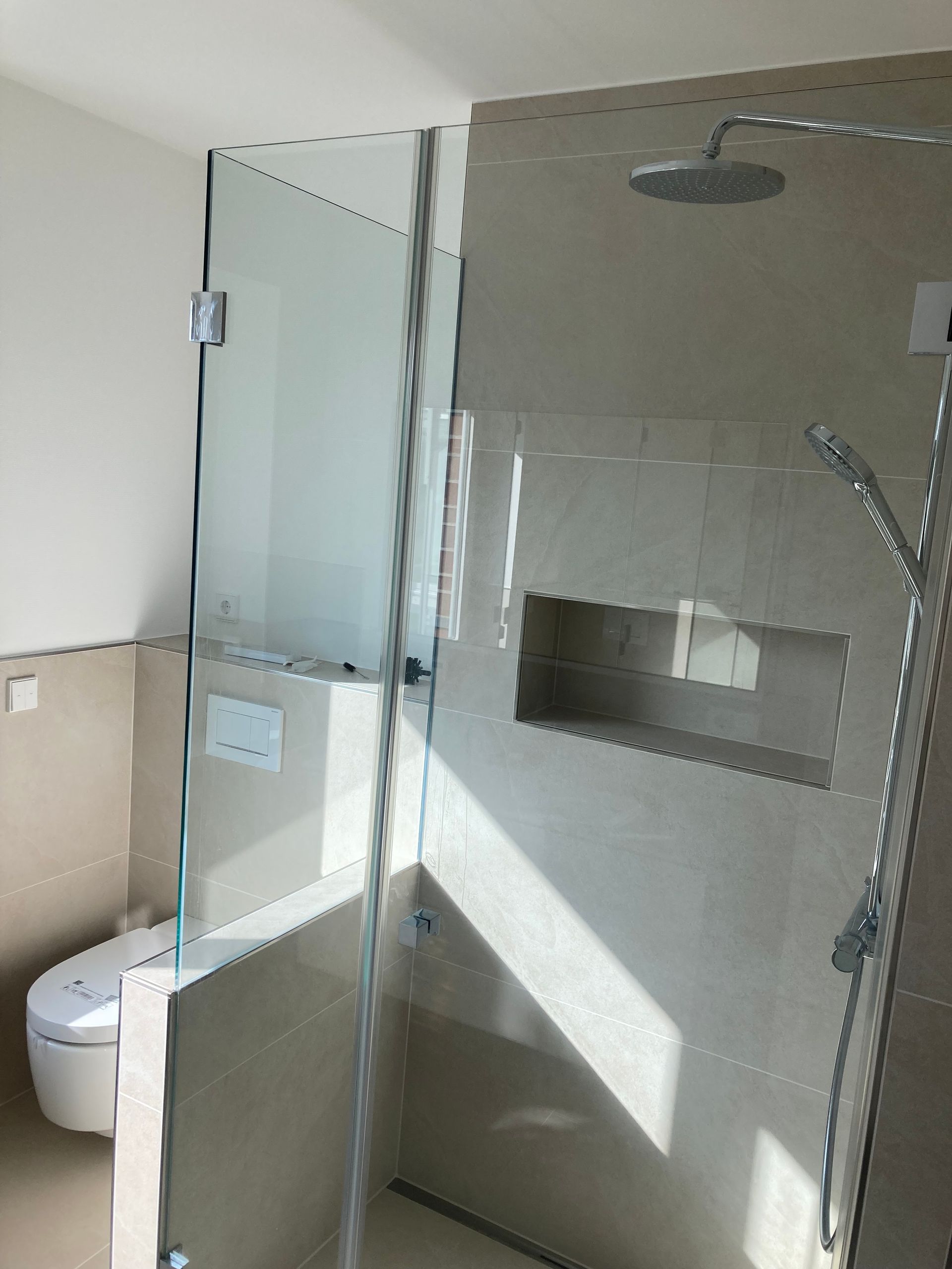 Badezimmerdusche mit Glastüren, beigen Fliesen und einer Toilette auf der linken Seite.