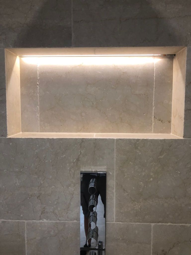 Eingelassenes Regal mit Deckenbeleuchtung in einer gefliesten Dusche und darunter ein Chromhahn.