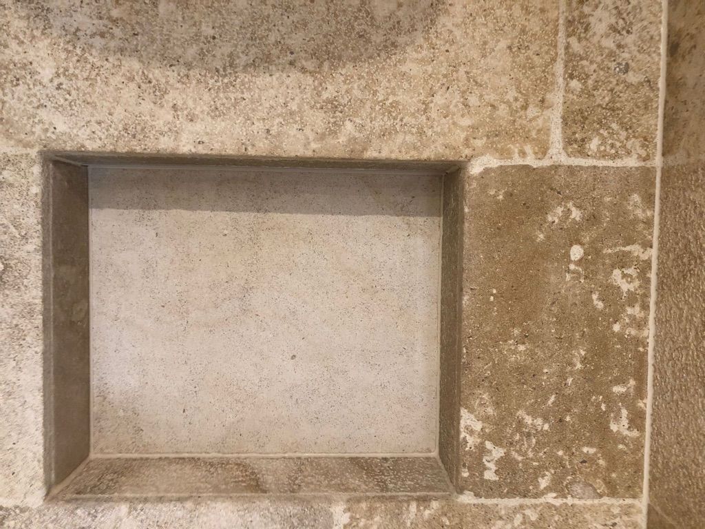 Eingelassenes rechteckiges Regal in einer beigen Steinwand mit sichtbaren Fliesenfugen.