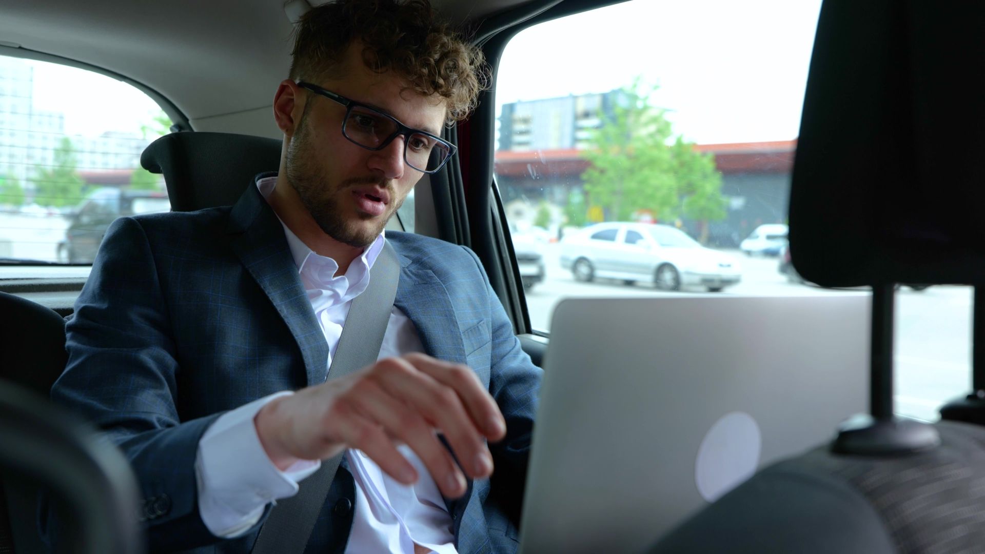 Un homme portant des lunettes travaille sur un ordinateur portable sur la banquette arrière d'une voiture.