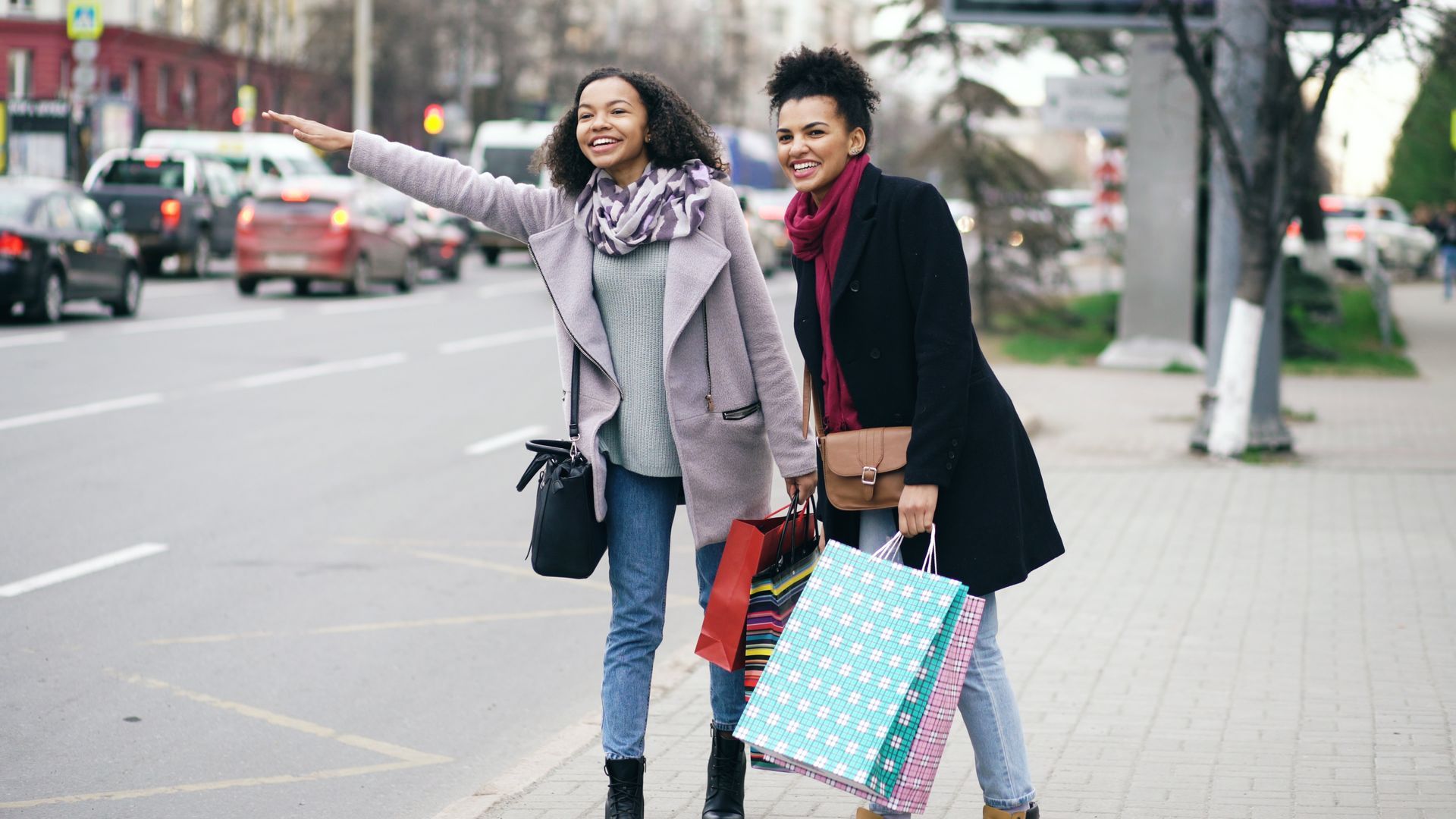 Deux femmes, sacs de shopping à la main, marchent sur un trottoir en ville.