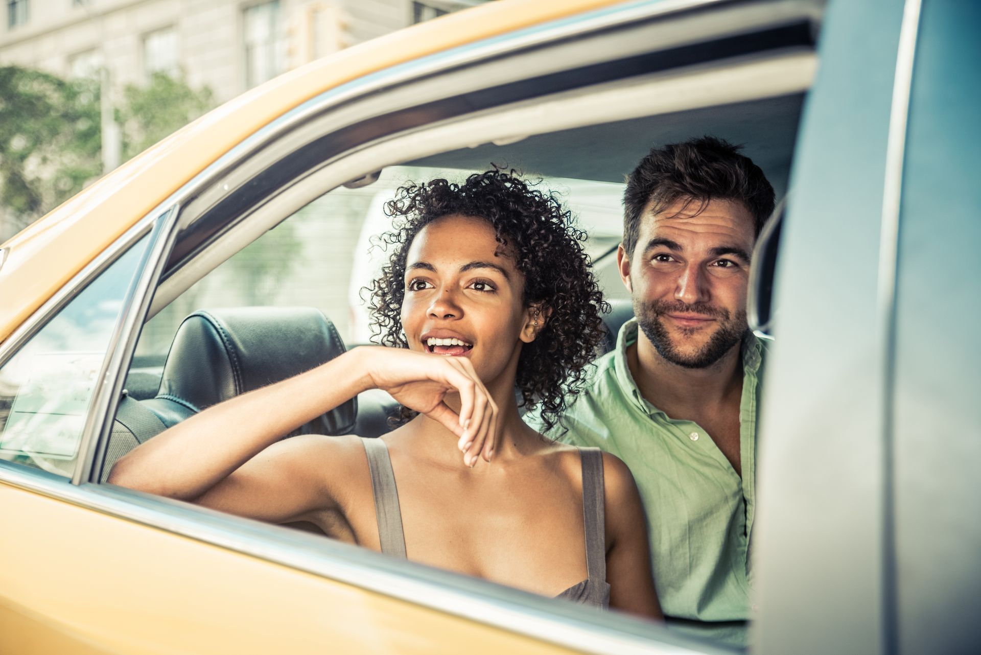 Deux personnes souriant à l'intérieur d'une voiture jaune, vues à travers la fenêtre ouverte