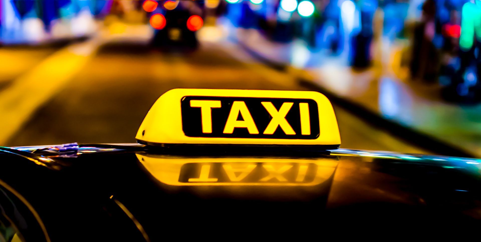 Panneau lumineux jaune de taxi sur le toit d'une voiture la nuit, avec les lumières de la ville floues en arrière-plan.