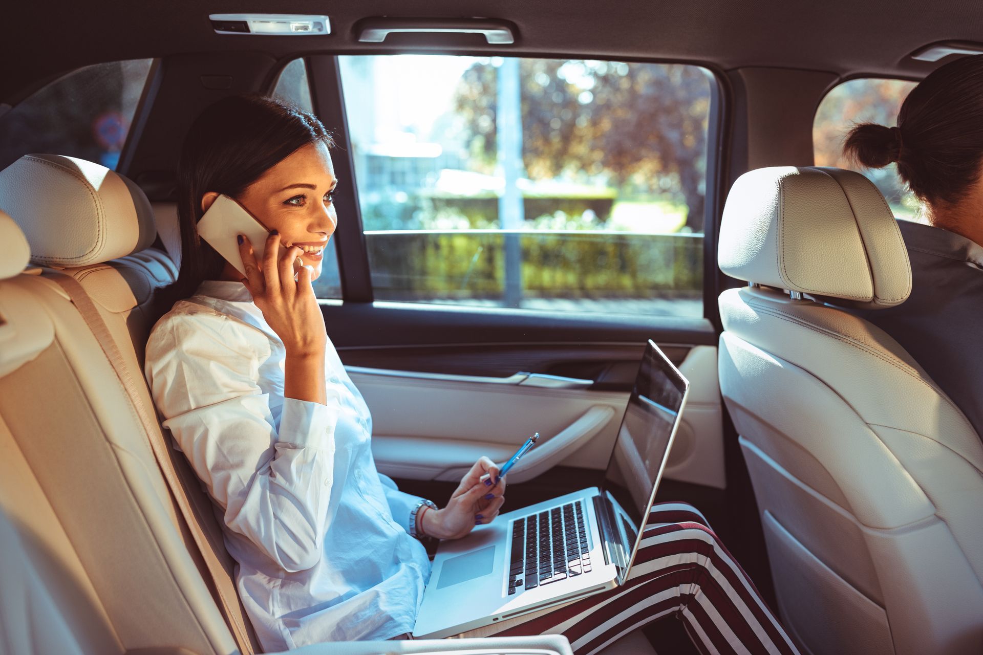 Une femme utilise un téléphone et un ordinateur portable sur la banquette arrière d'une voiture.
