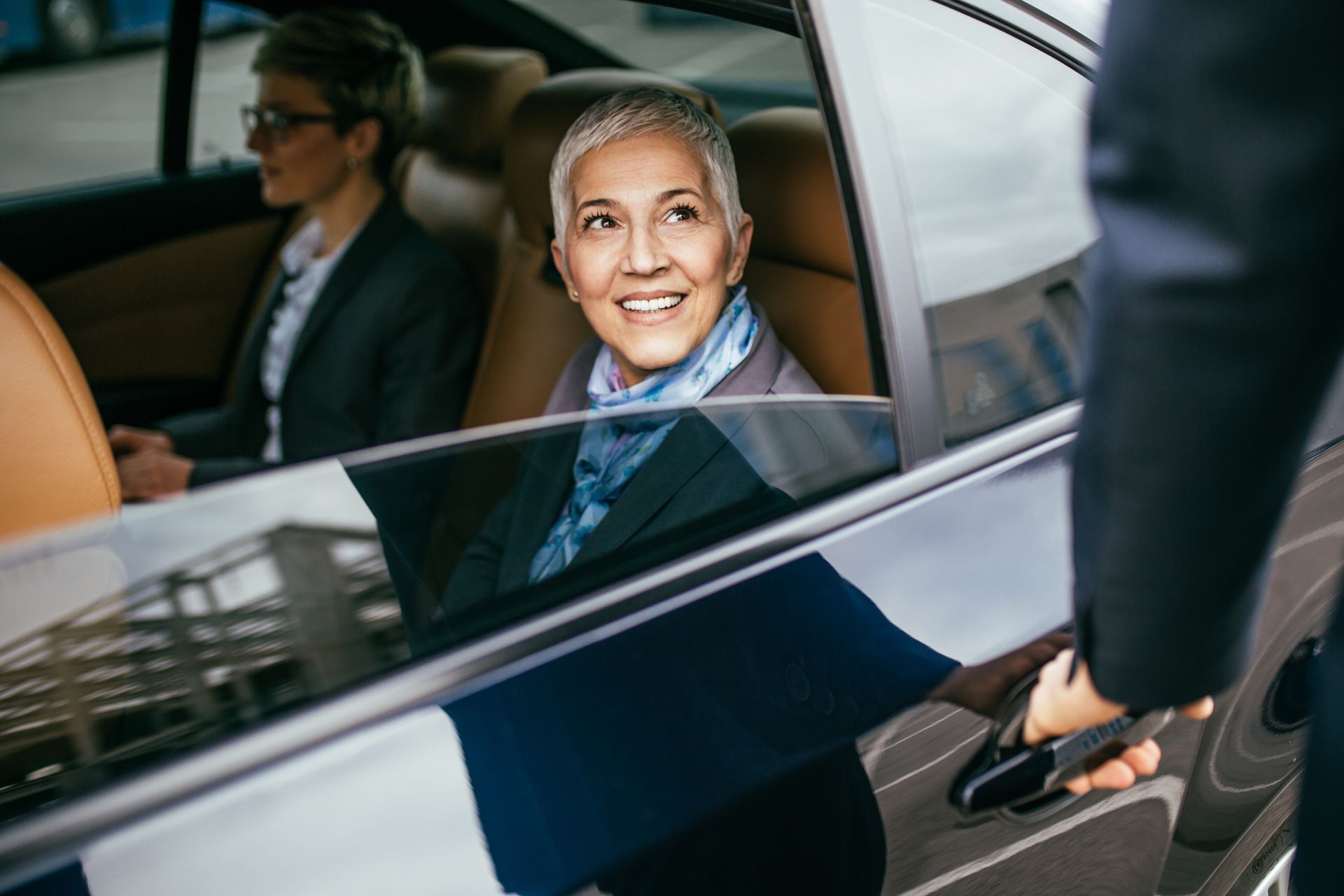 Une femme sourit dans une voiture tandis que quelqu'un ouvre la portière à l'extérieur.