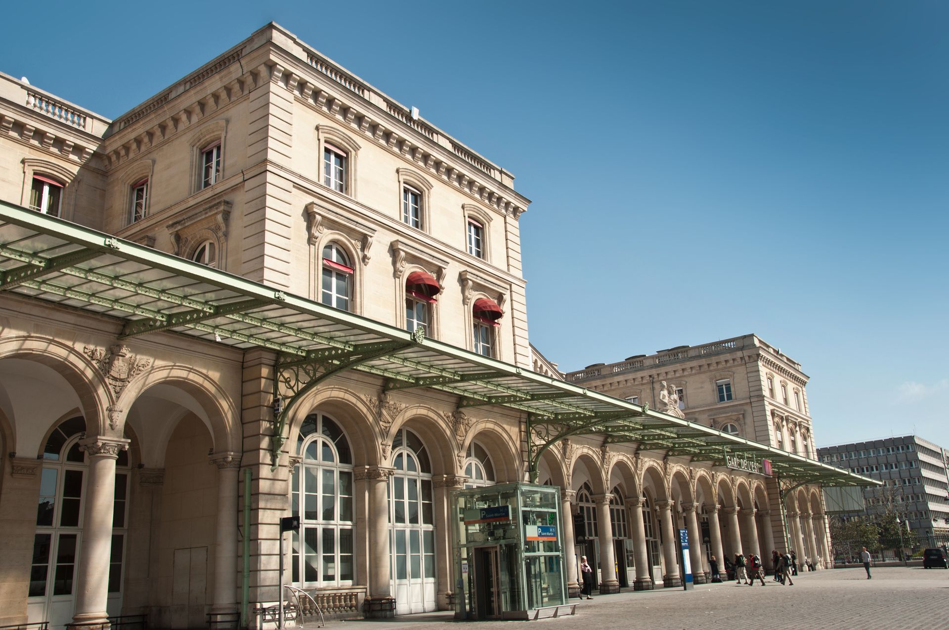 Gare historique avec colonnade, voûtes et auvents sous un ciel bleu clair.