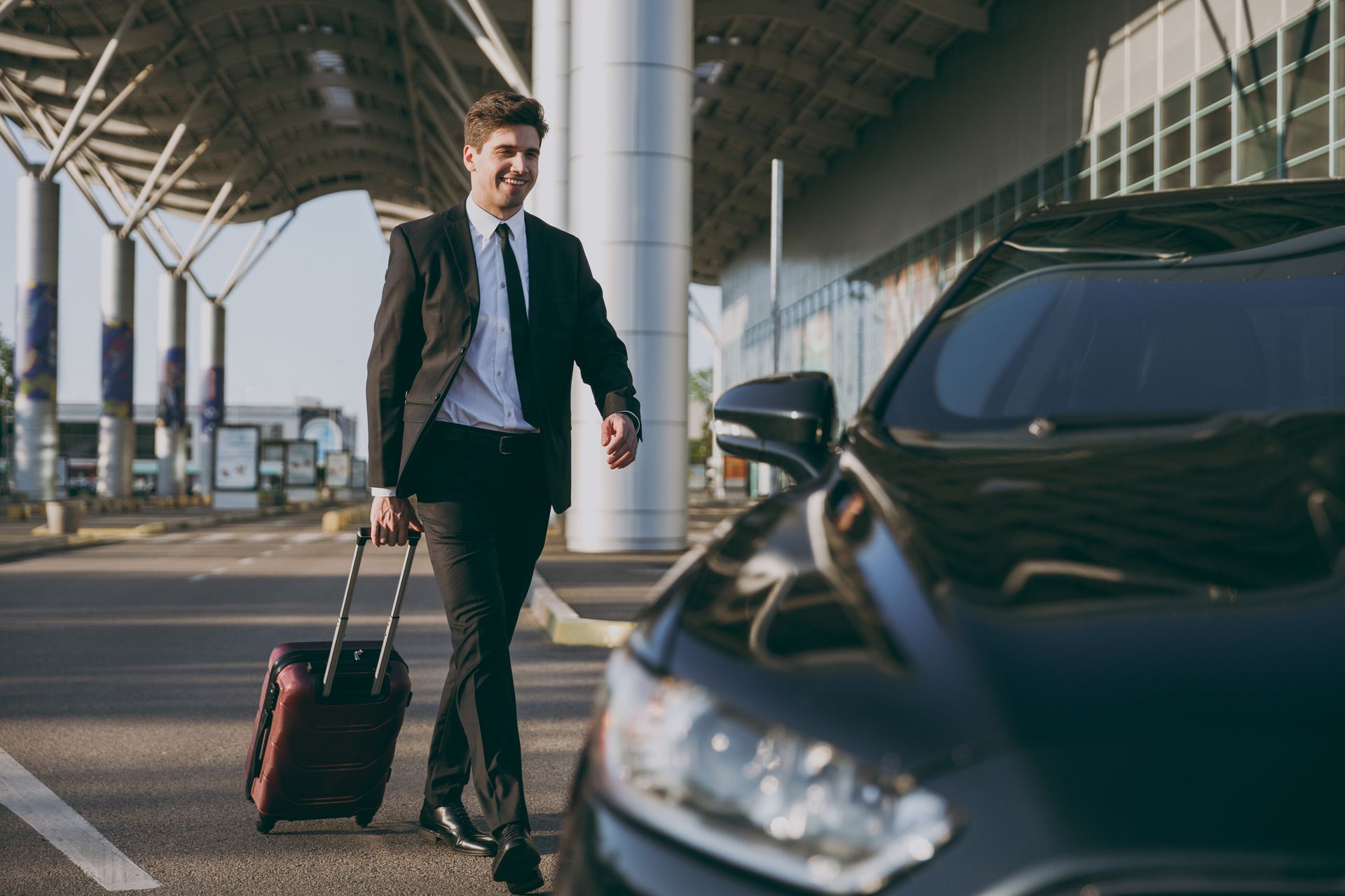 Un voyageur marchant avec une valise vers une voiture noire dans un terminal d'aéroport.