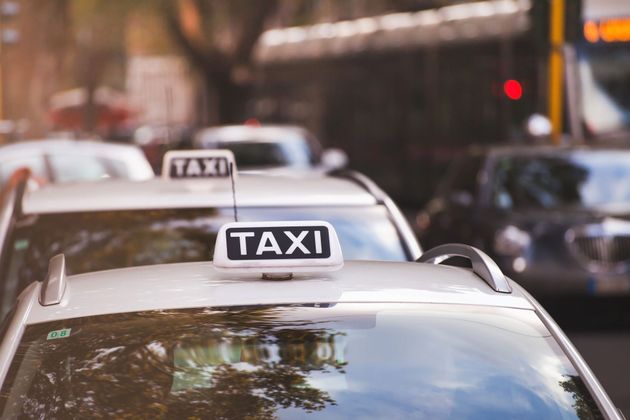 Filet de taxis blancs dans la circulation urbaine, avec des panneaux publicitaires sur les toits et une rue en arrière-plan flou.