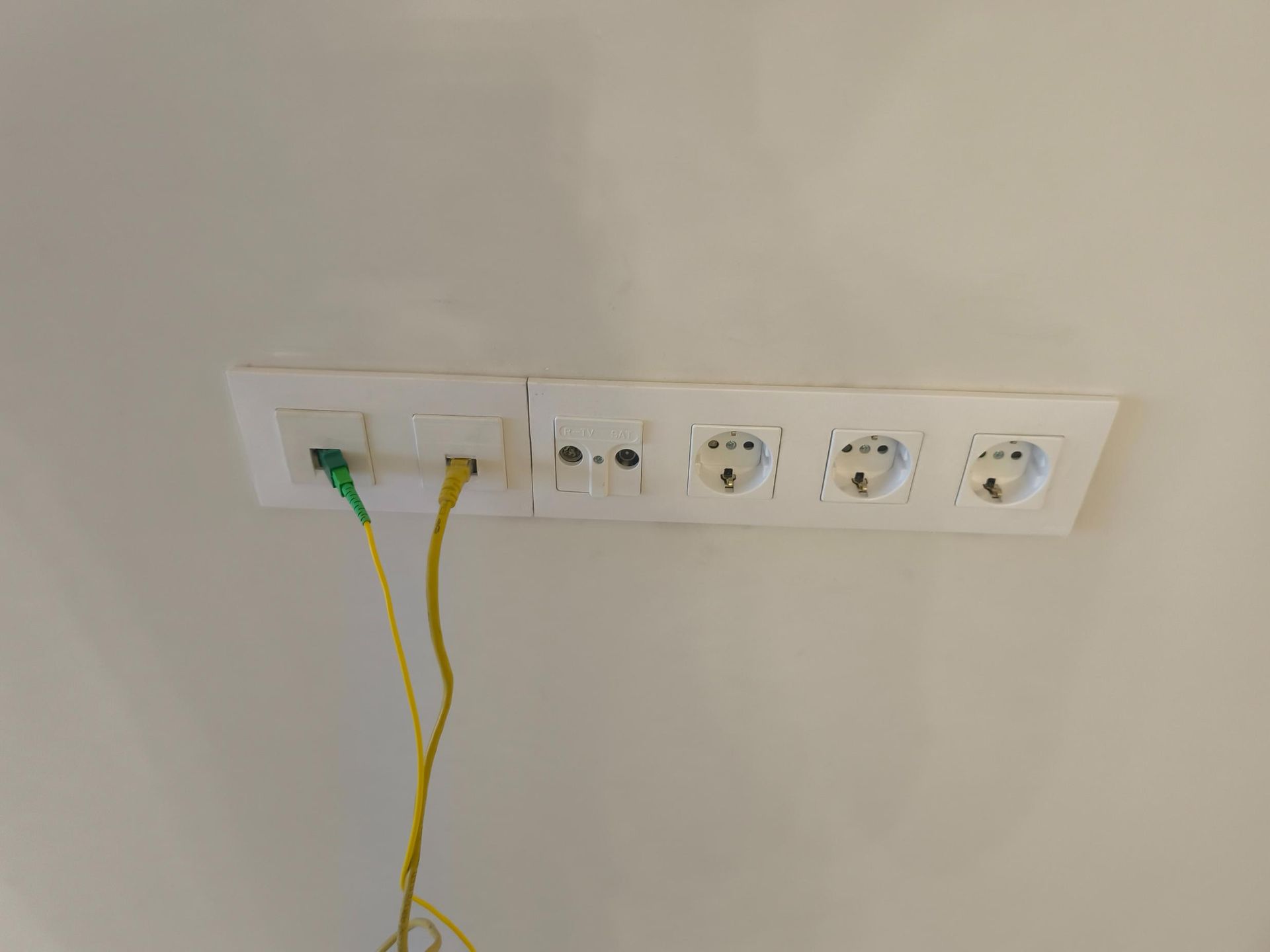 Panel de toma de corriente con cables amarillos y verdes enchufados sobre una pared beige.