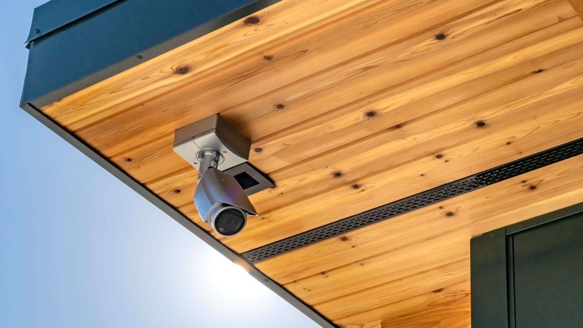 Cámara de seguridad instalada bajo un alero de madera contra un cielo azul