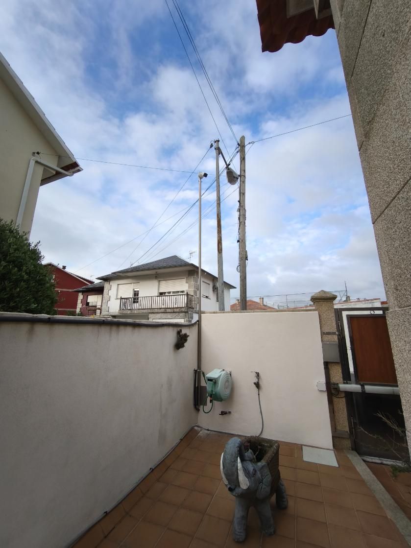 Pequeño patio con suelo de baldosas, puerta abierta, postes de luz en lo alto y un perro en primer plano.