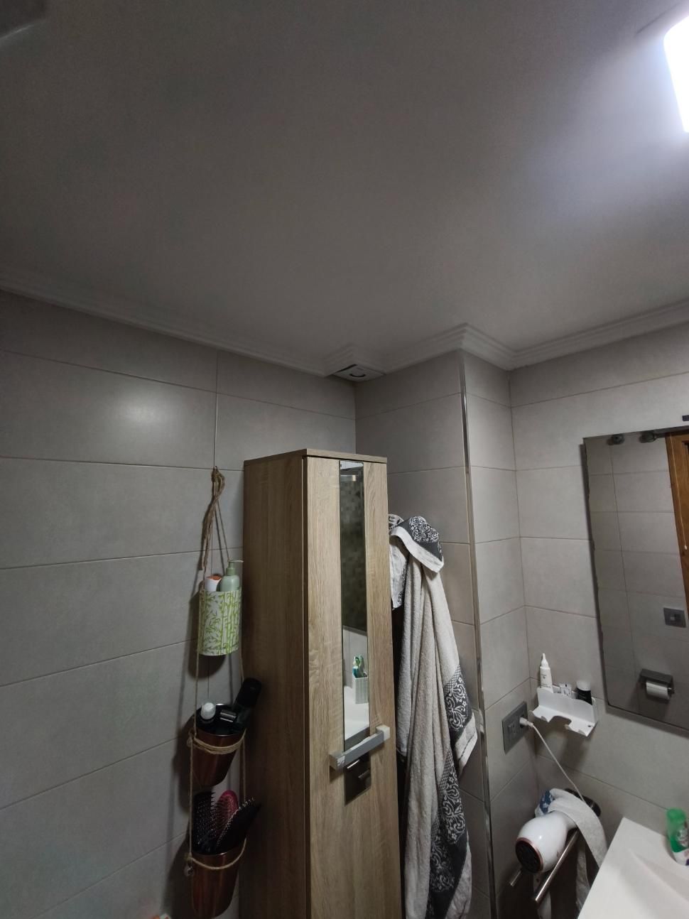 Baño pequeño con paredes alicatadas en color beige, zona de ducha, toallas colgadas