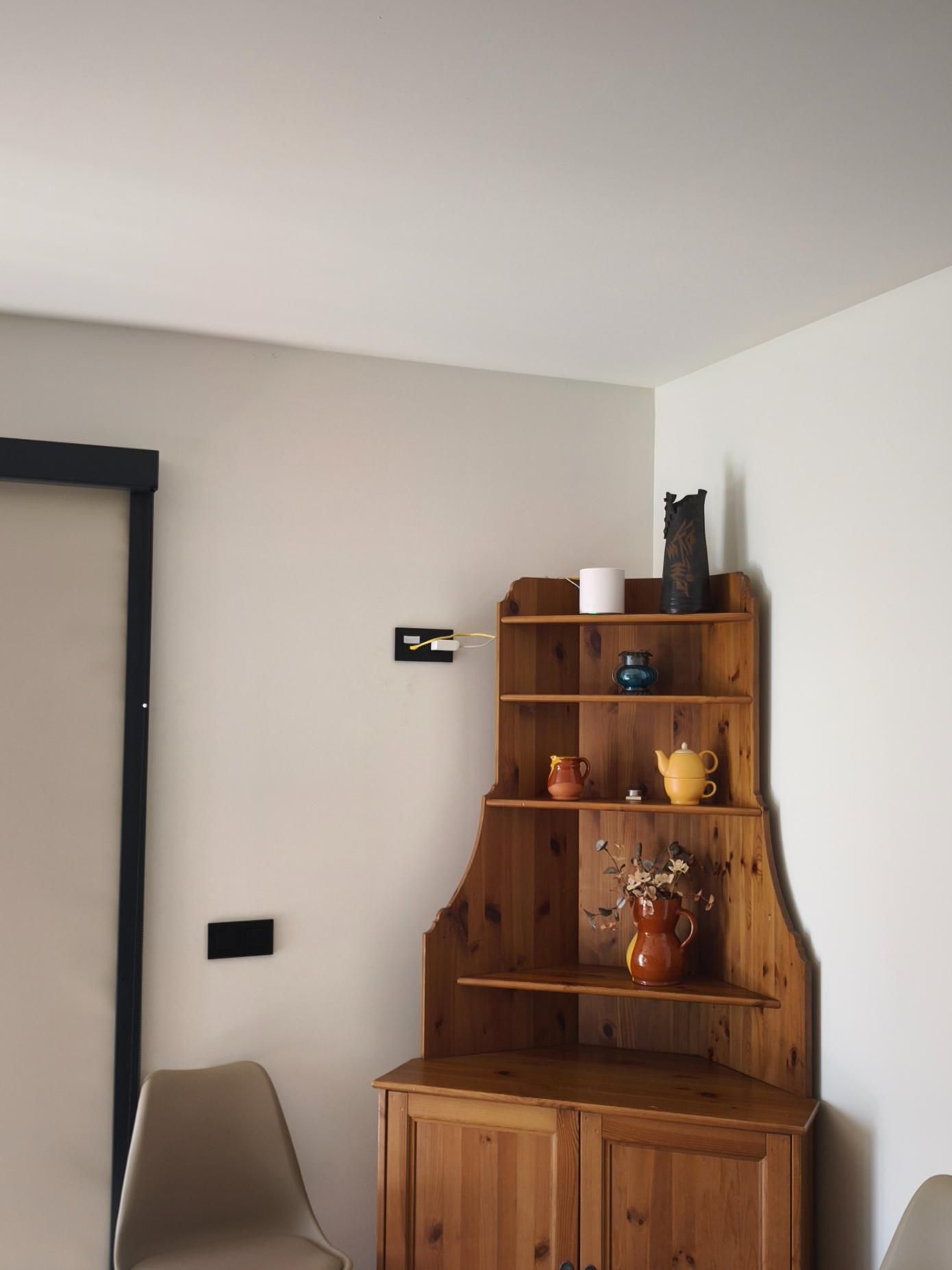 Armario esquinero de madera con cerámica decorativa en una habitación luminosa de paredes blancas.