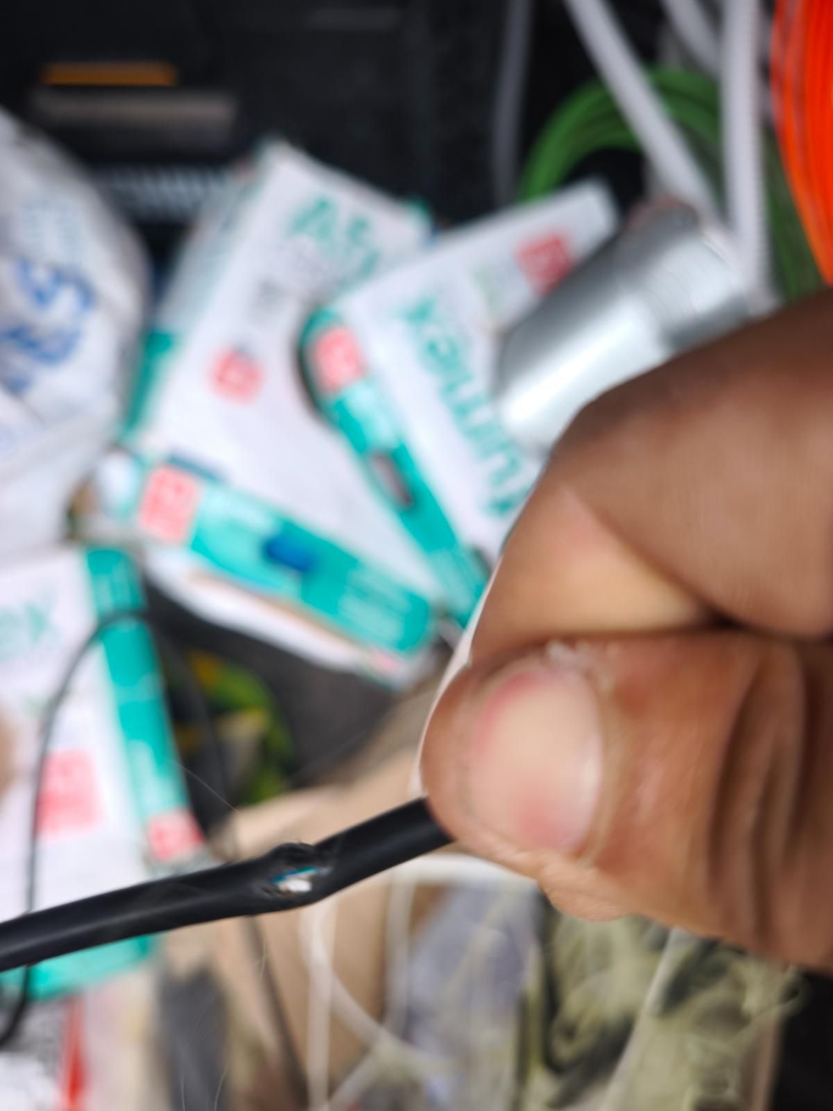 Una mano sostiene un cable negro cerca de un montón de tubos de pasta de dientes y otros artículos de aseo personal.