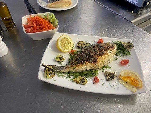 Ein weißer Teller mit Fisch und Gemüse auf einem Tisch.