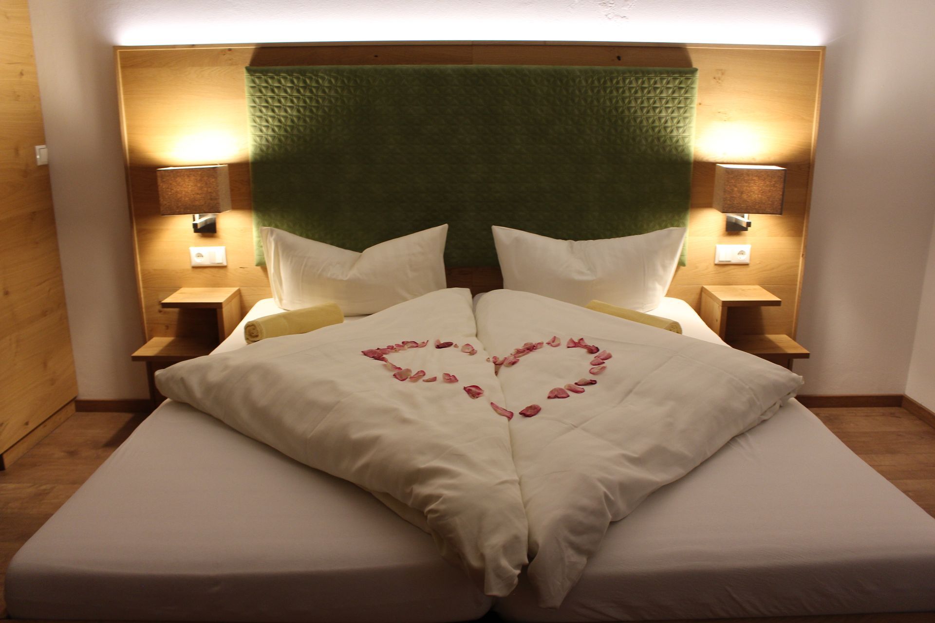 Doppelbett mit grünem Kopfteil, Herz aus Blüten auf der weißen Bettwäsche