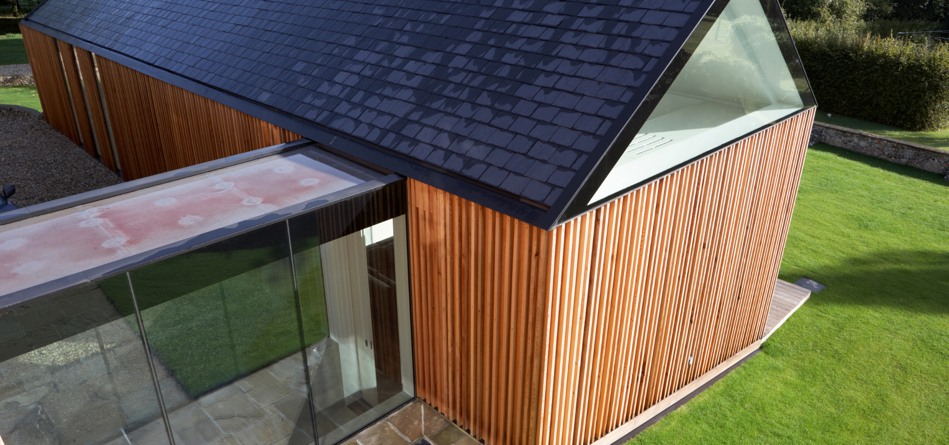 Bâtiment moderne avec façade en bois, toit sombre et fenêtres en verre. Situé sur un espace vert.