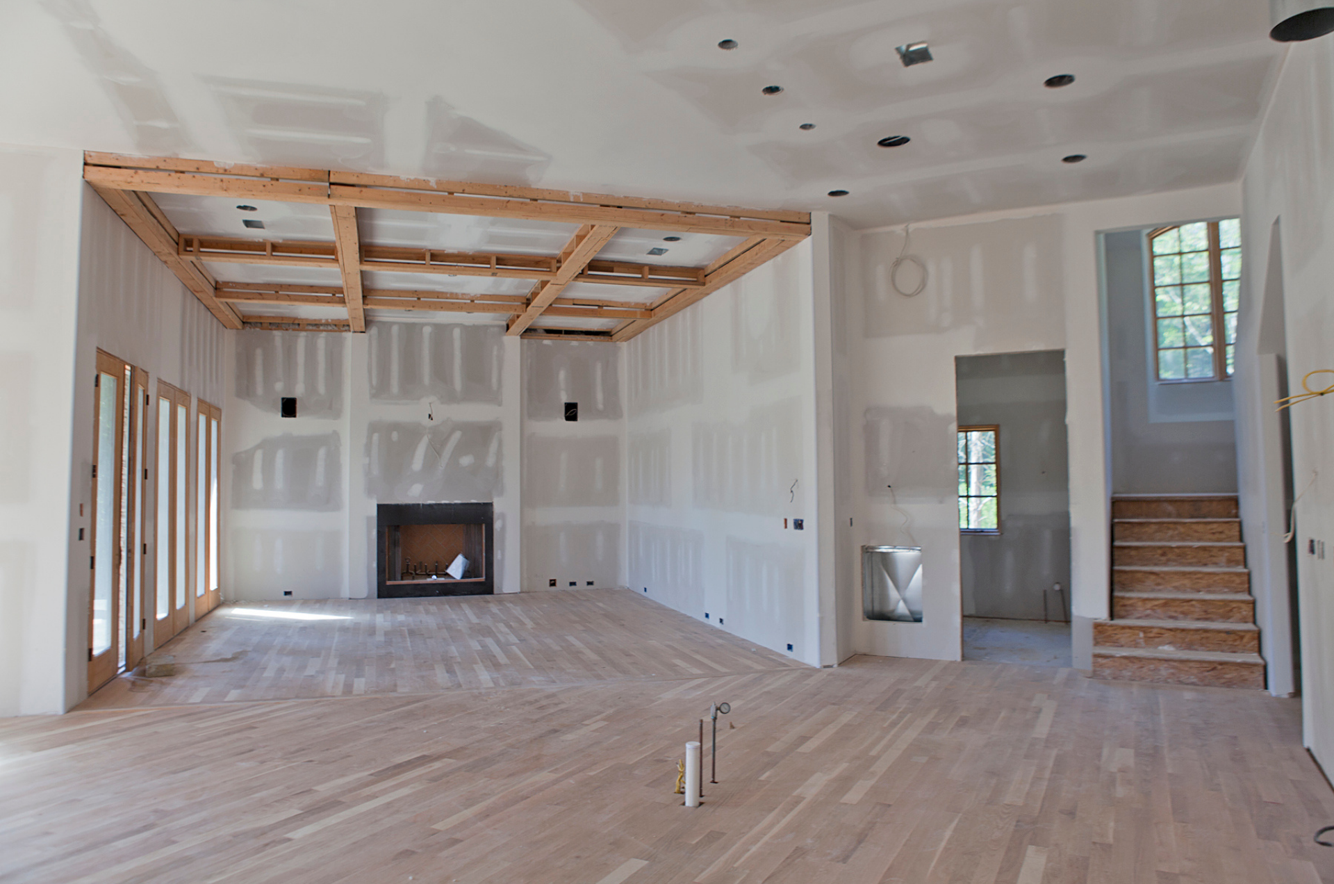 Intérieur d'une pièce en construction, avec poutres en bois apparentes, cloisons sèches, cheminée et parquet.