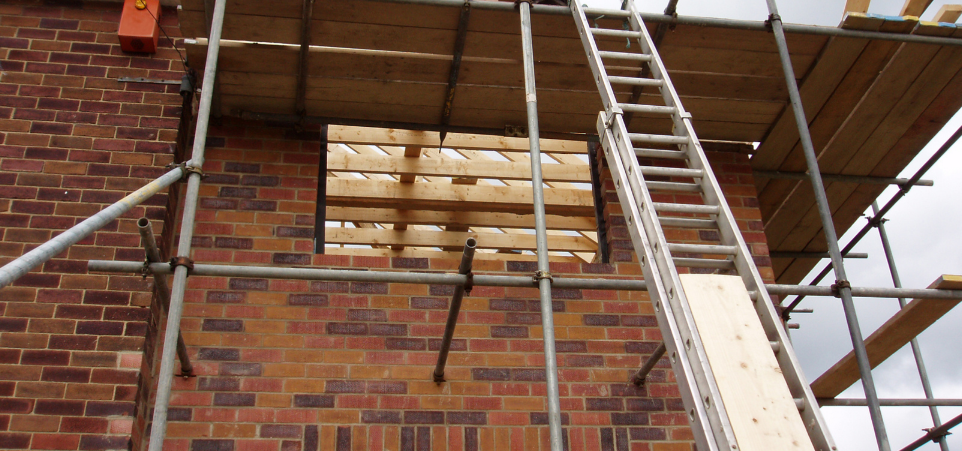 Mur de briques avec fenêtre barricadée, échafaudage et échelle.