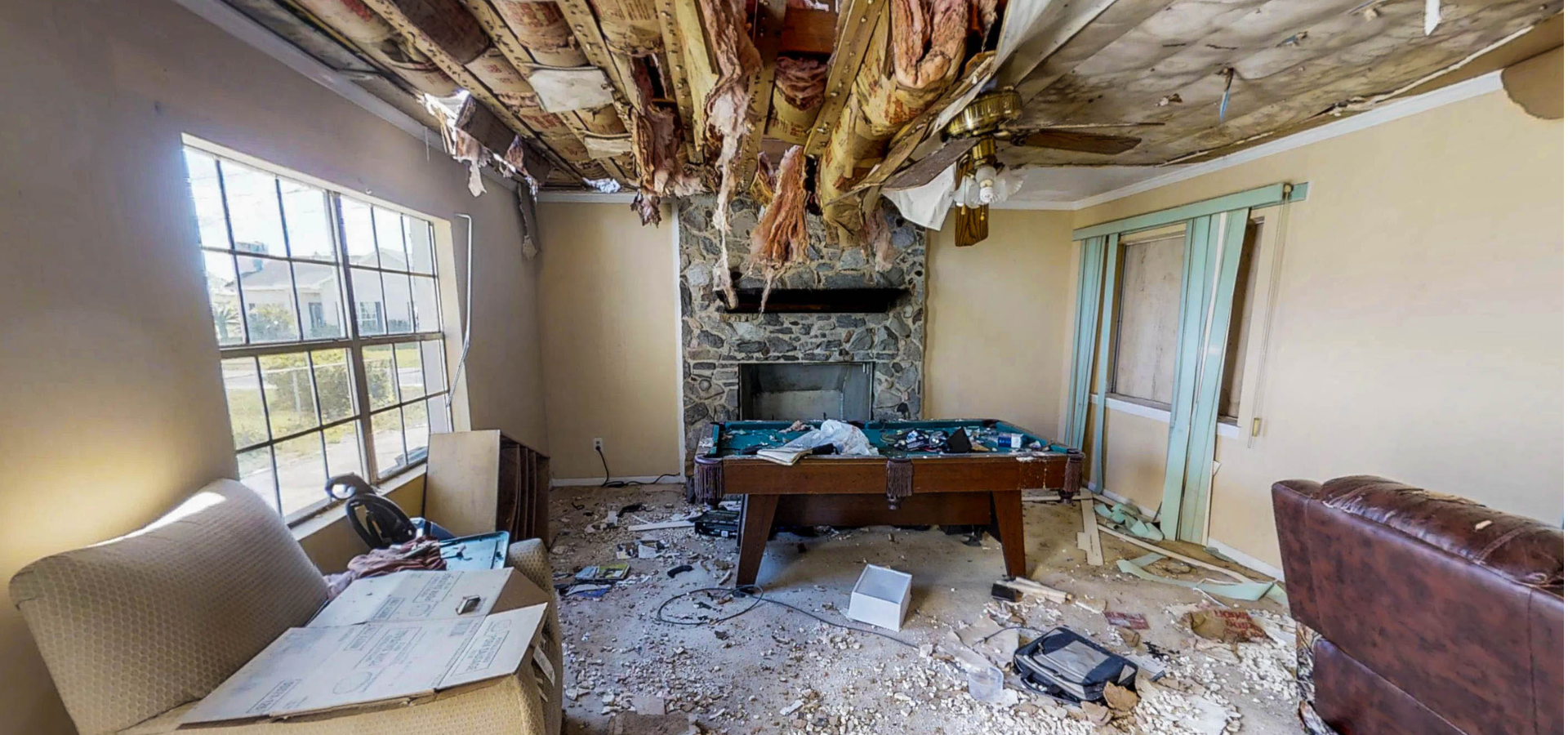 Vue intérieure d'une pièce endommagée. Le plafond s'effondre. On y trouve un billard et une cheminée.