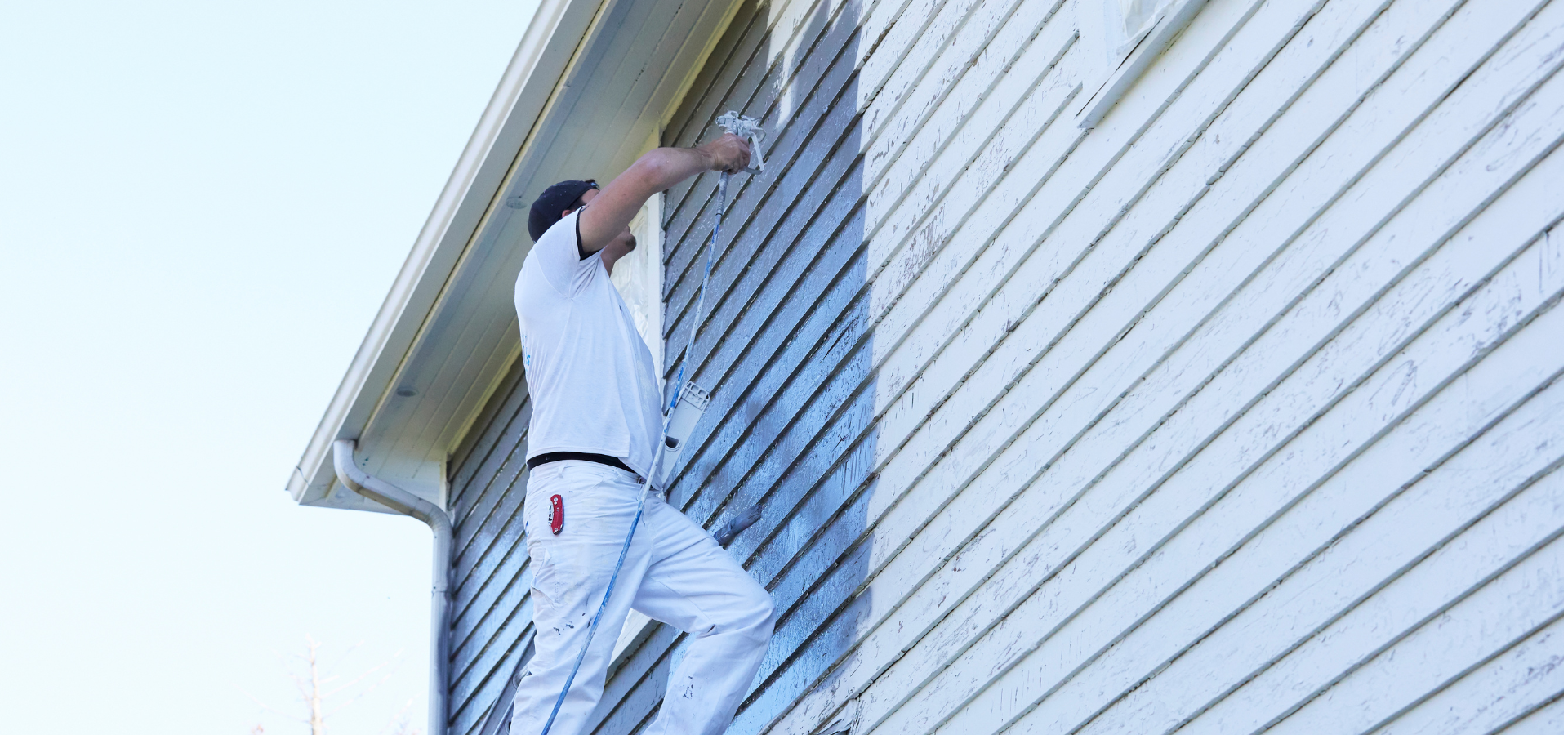 Une personne peint le côté d'une maison en blanc tout en se tenant debout sur une échelle.