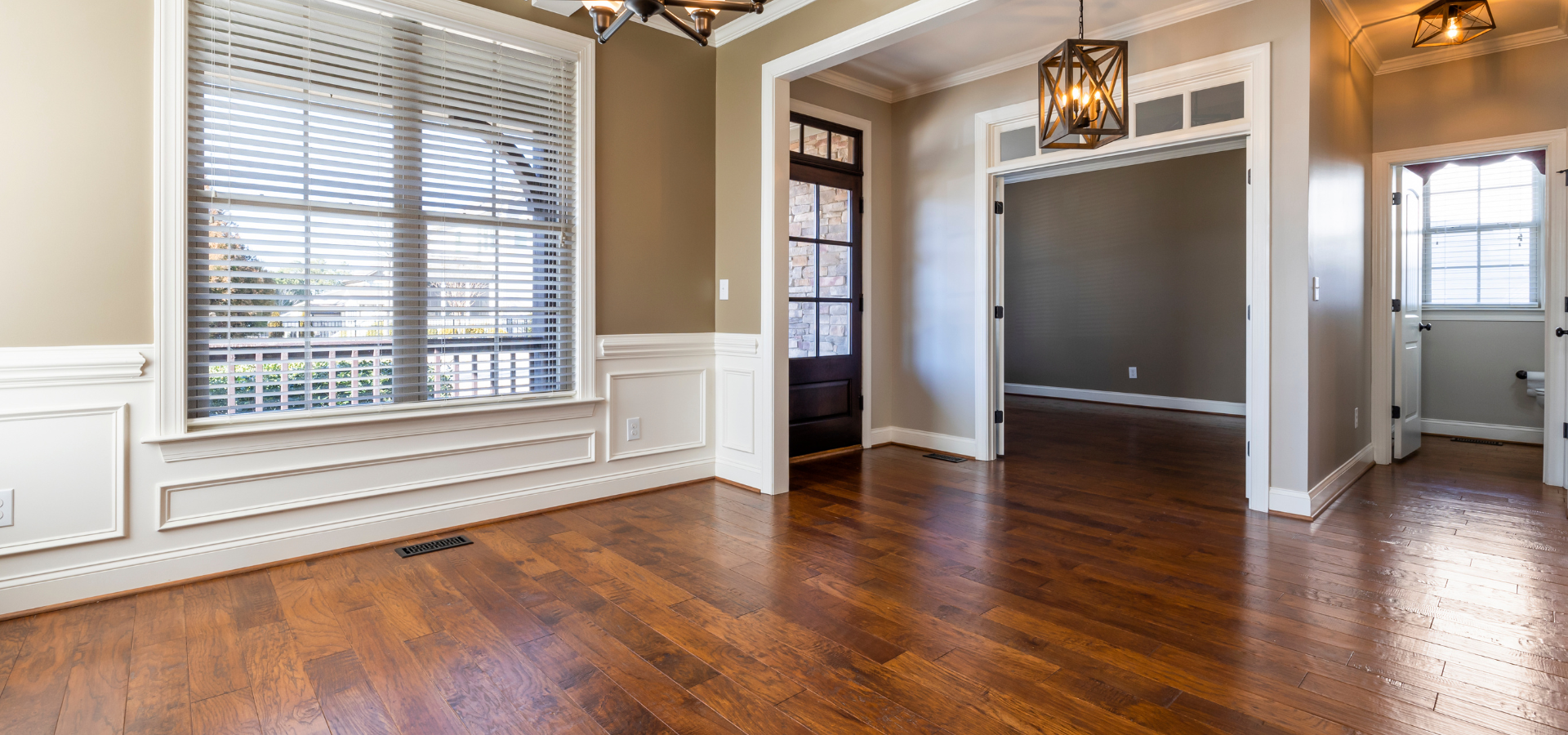 Salle à manger vide avec plancher en bois, grande fenêtre et portes cintrées.