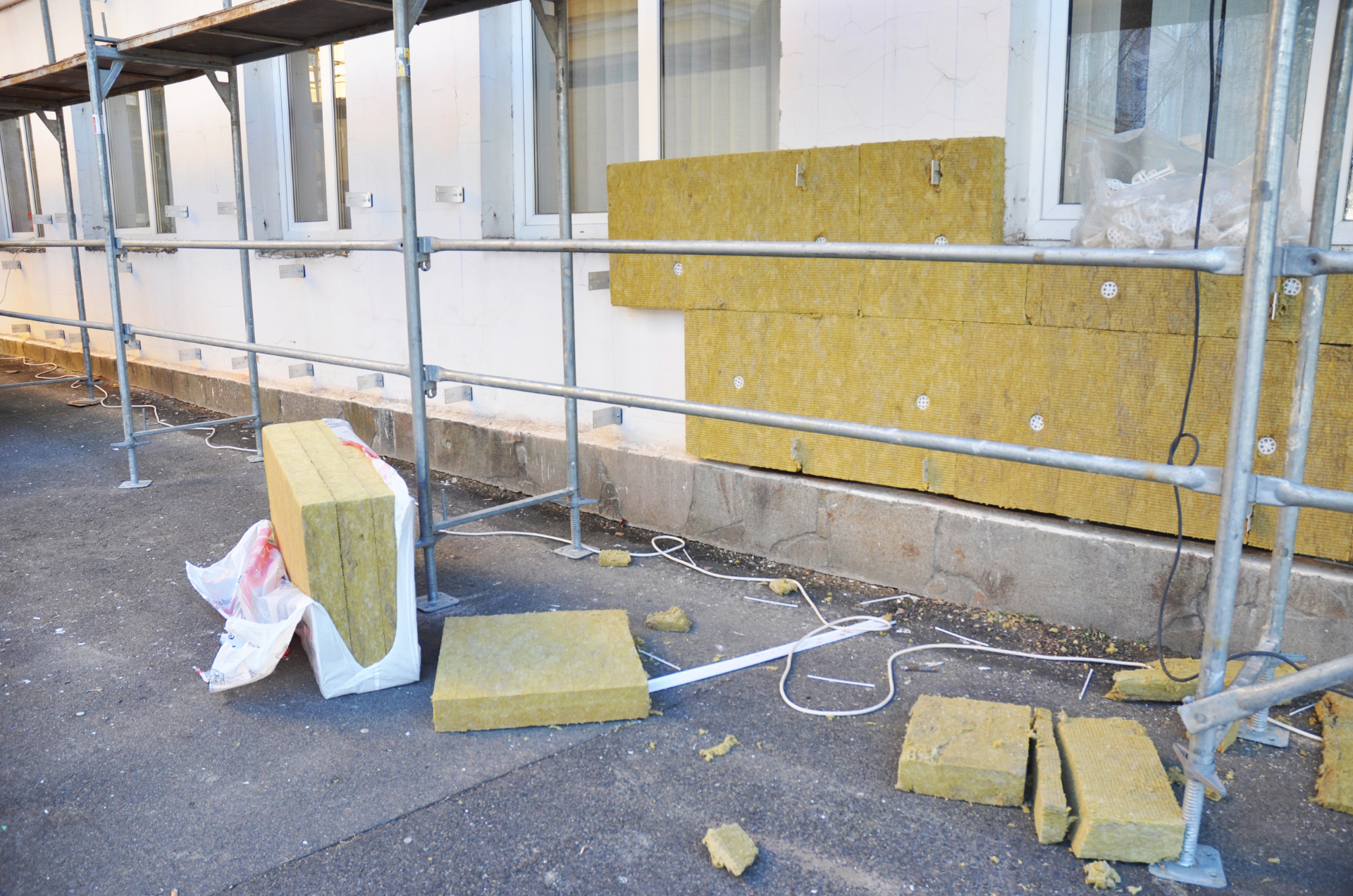 Pose d'isolation de murs extérieurs, chantier. Panneaux isolants jaunes, échafaudage, bâtiment avec fenêtres.