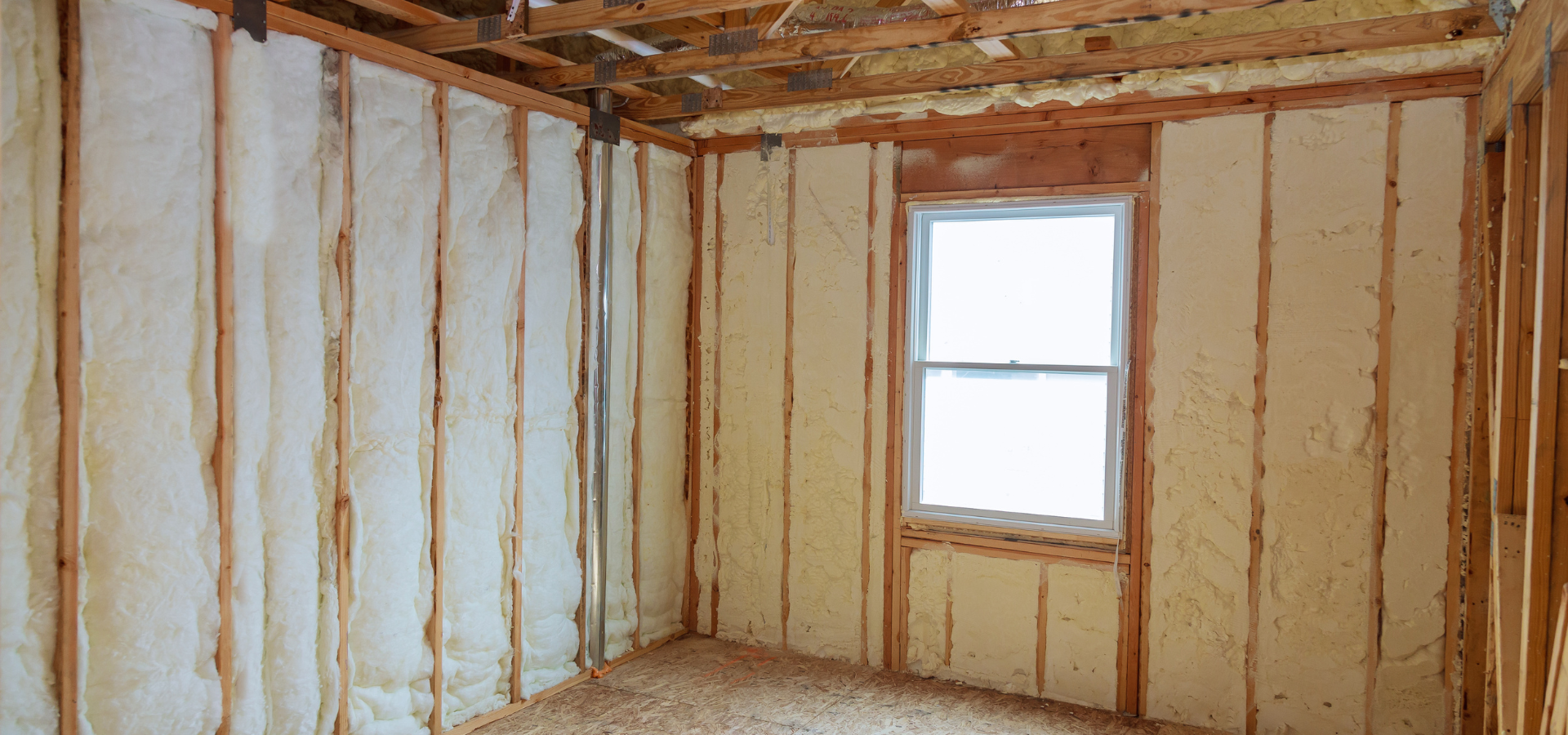 Intérieur d'une pièce avec isolation en mousse pulvérisée entre des montants en bois et une fenêtre.