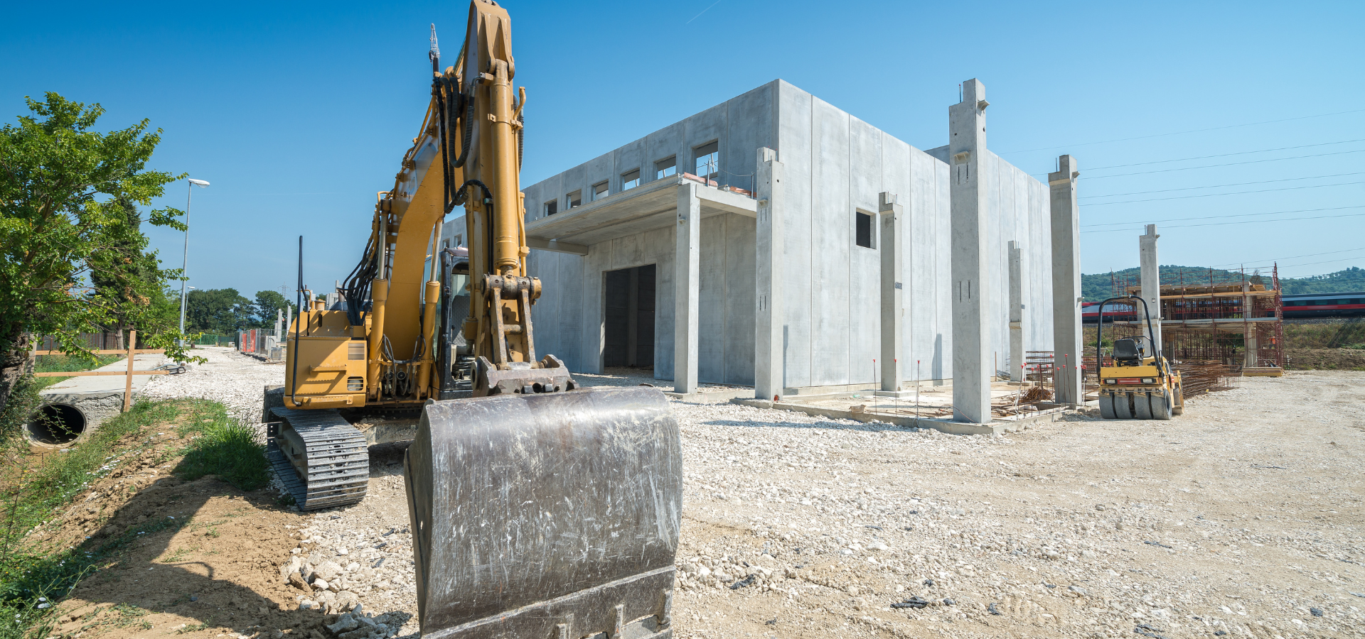 Chantier de construction avec excavatrice et bâtiment en béton inachevé sous un ciel bleu clair.
