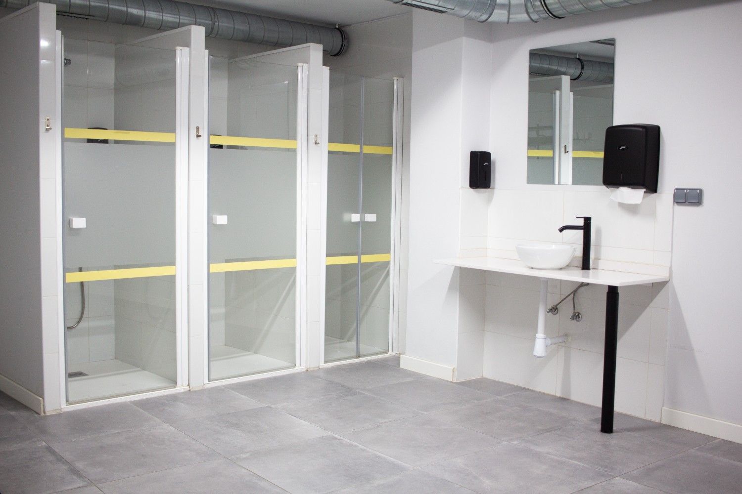 Baño moderno con tres cubículos, un lavabo blanco y un dispensador de jabón negro sobre 