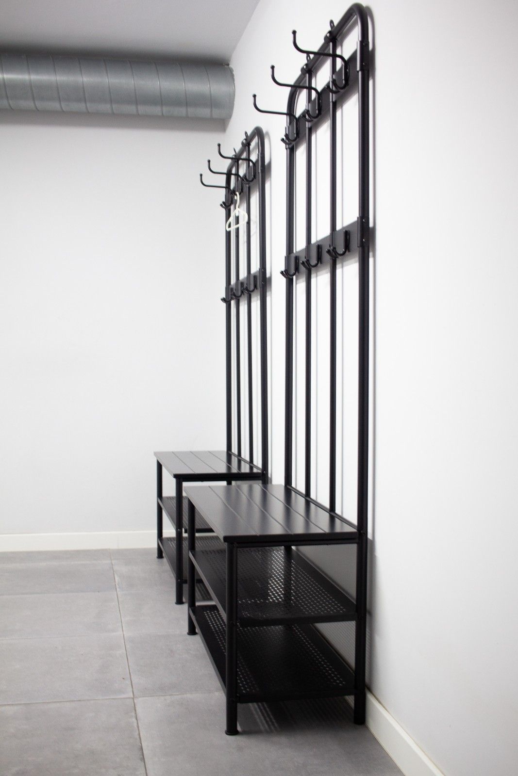 Banco perchero de metal negro con estantes en un pasillo minimalista con paredes blancas.