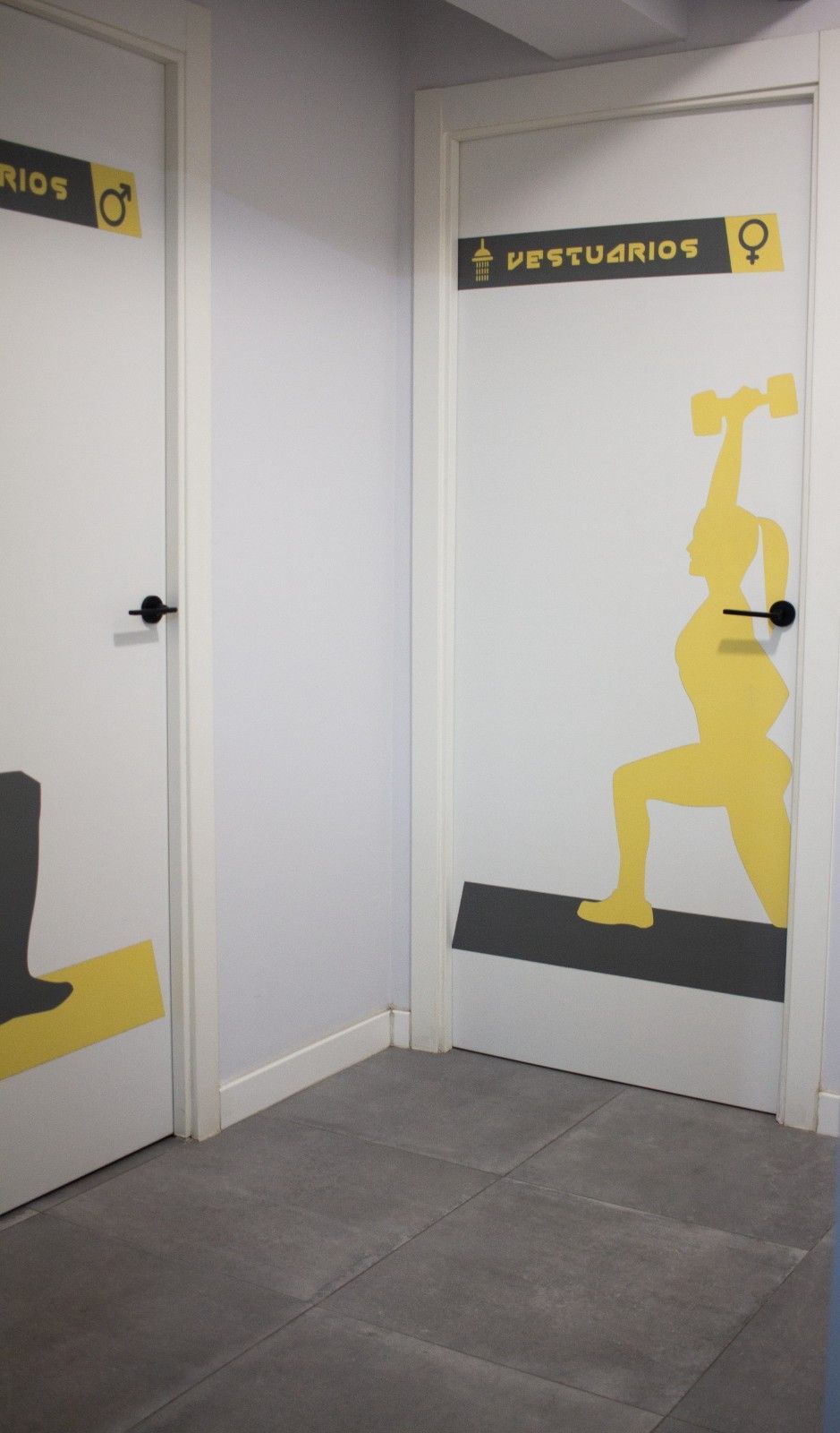 Pasillo blanco con dos puertas etiquetadas como “Restringido” y gráficos de advertencia en amarillo.